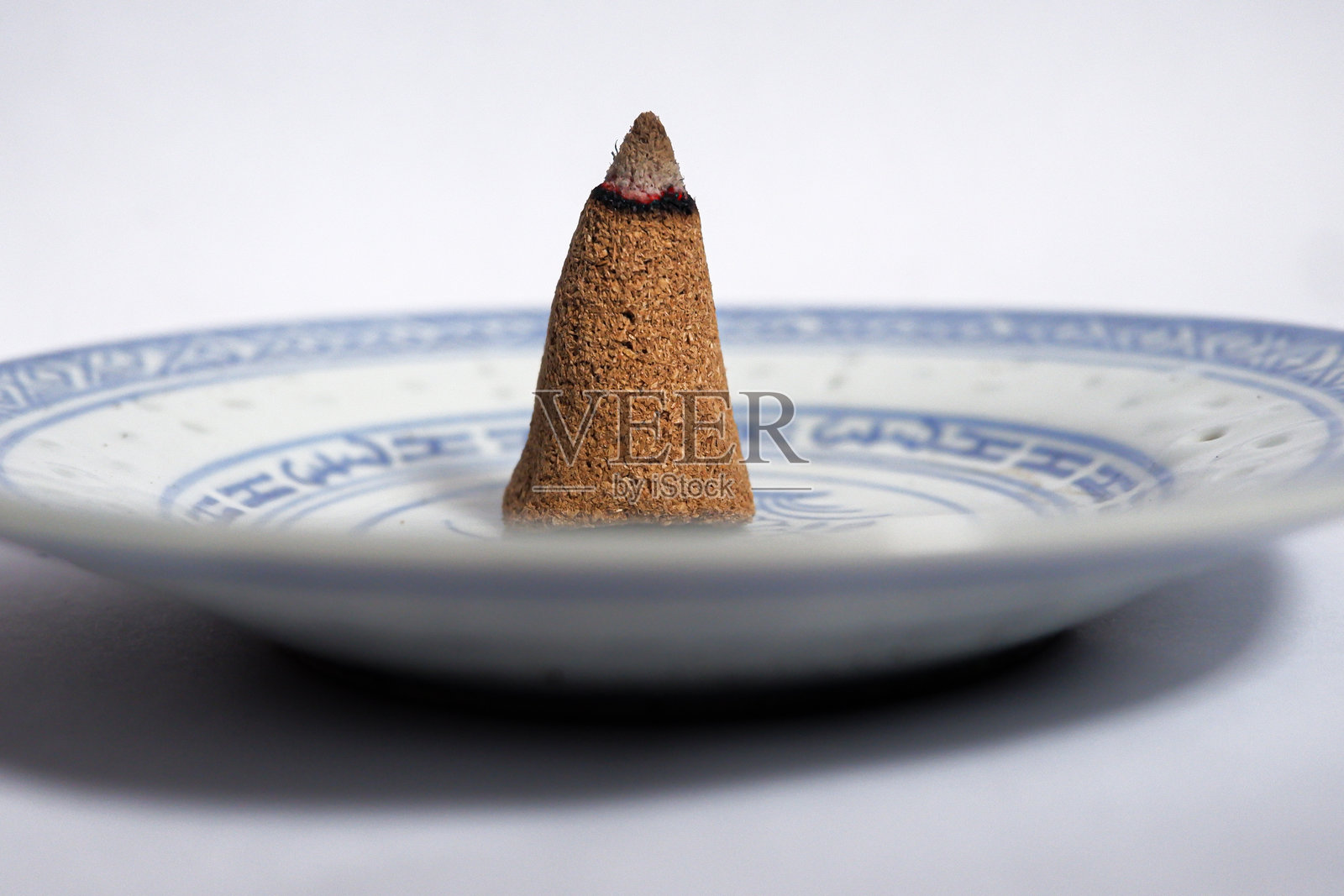 一个燃烧的香锥放在小盘子上，背景为白色。照片摄影图片