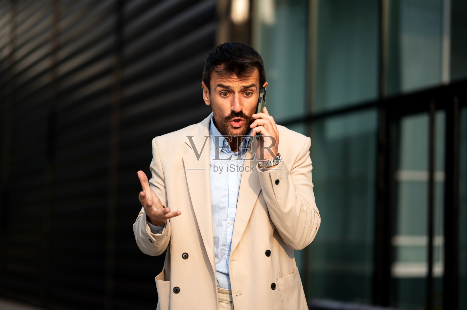 中年商人在商业大楼前站着，使用智能手机进行沟通。照片摄影图片