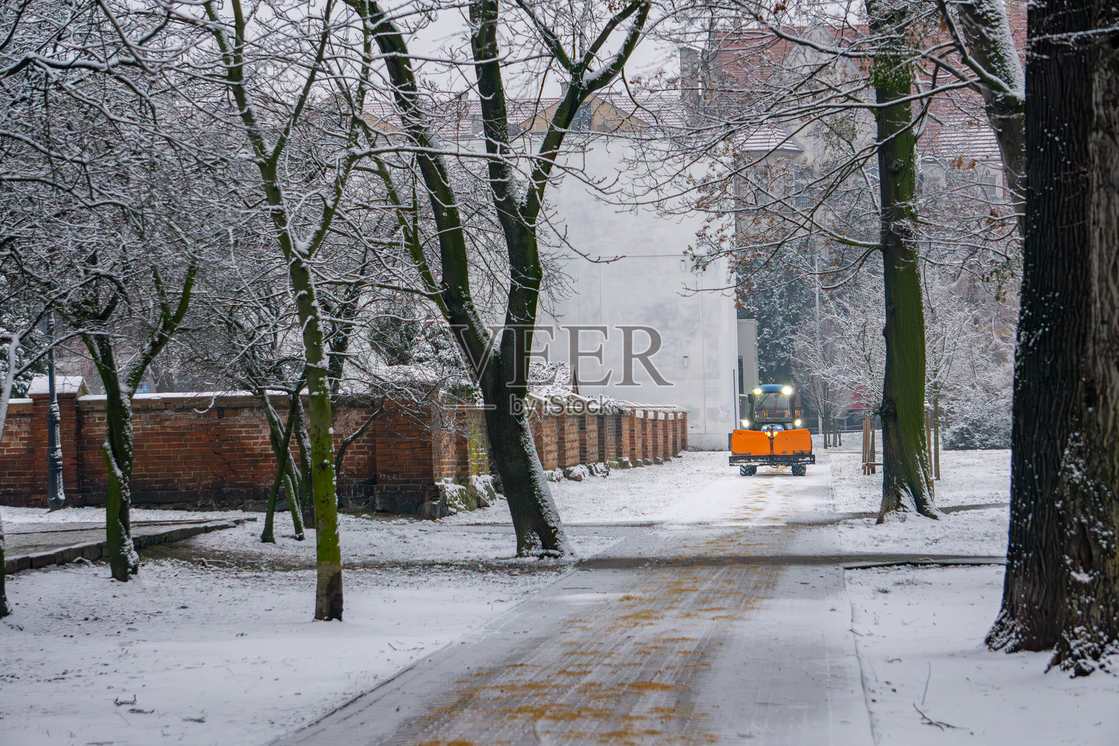 冬季城市街道上驾驶带有铲雪机的拖拉机。拖拉机在街道上行驶，呈现运动效果。冬季道路的除雪和城市公园的撒沙。照片摄影图片