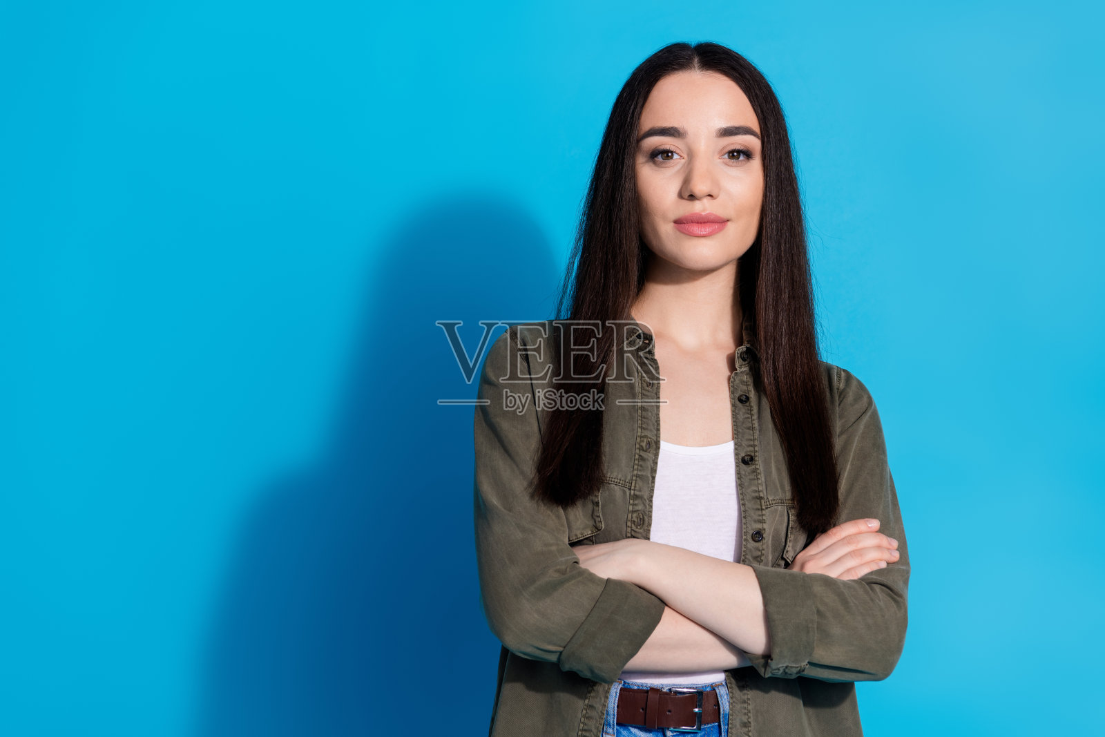 自信的棕发女性穿着休闲服，双臂交叉，背景为明亮的蓝色。照片摄影图片