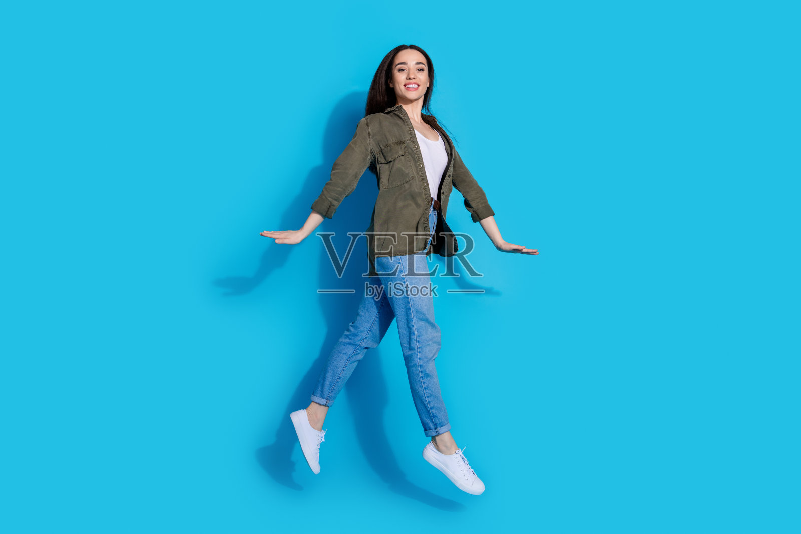 穿着时尚休闲服的快乐女性在明亮的蓝色背景下跳跃照片摄影图片