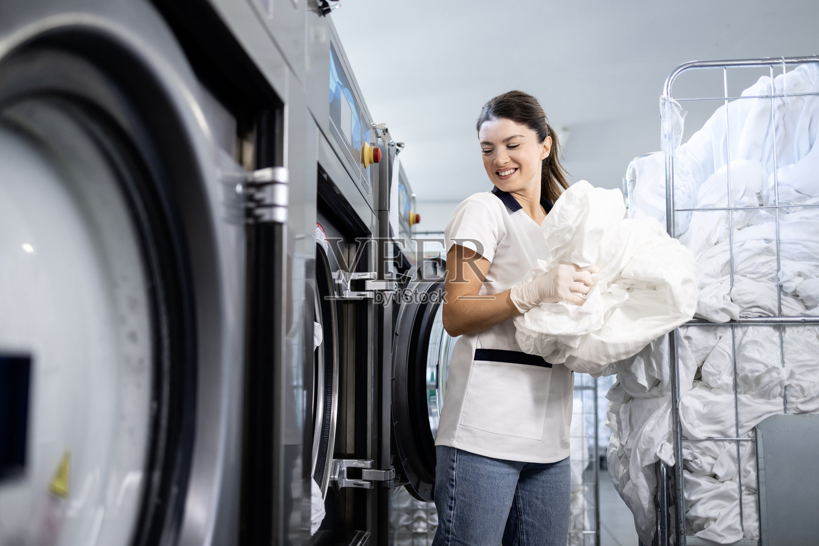 女性洗衣工站在工业洗衣机前。照片摄影图片