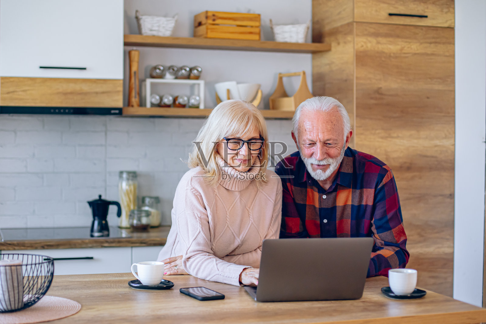 老年夫妇在厨房里一边喝咖啡一边使用笔记本电脑放松。照片摄影图片
