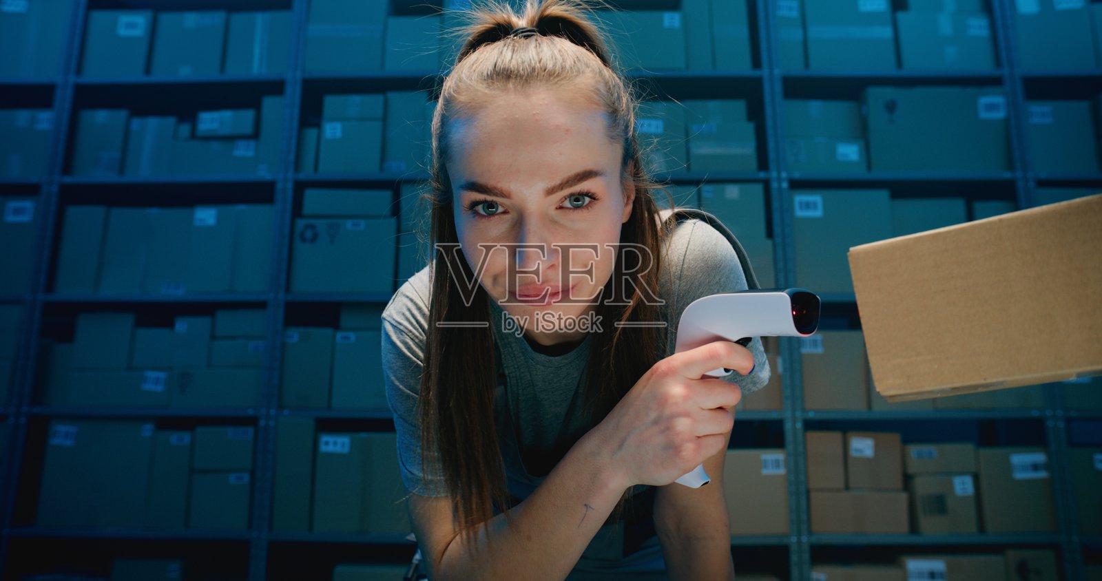 疲惫的女性物流专员望向镜头，正在仓库中用扫描仪扫描纸箱照片摄影图片