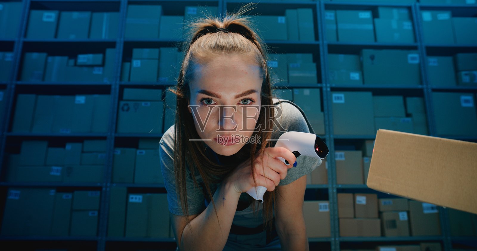 疲惫的女性仓库员工看着镜头，使用扫描仪扫描纸箱照片摄影图片