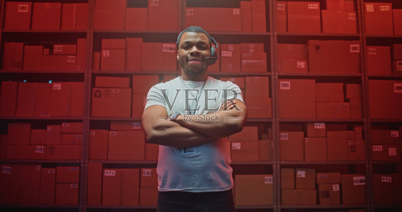在仓库中微笑并看向镜头的非裔美国物流专家，佩戴耳机。照片摄影图片