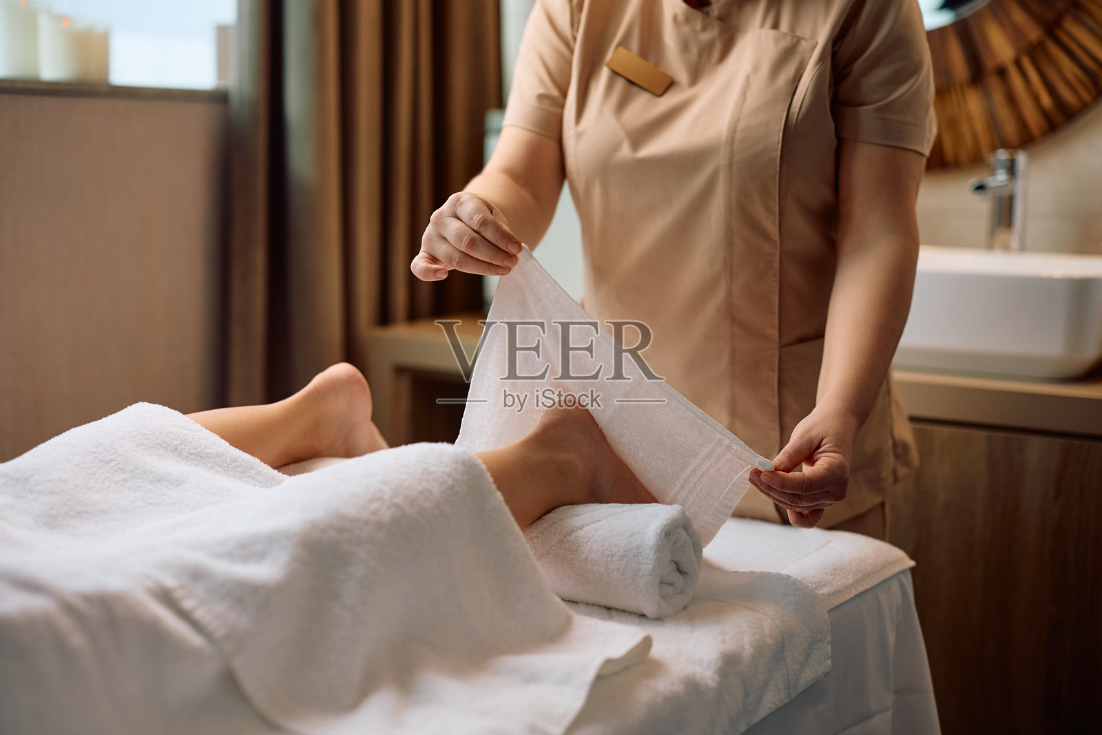 水疗中心治疗师在足部按摩时使用温暖的毛巾特写。照片摄影图片