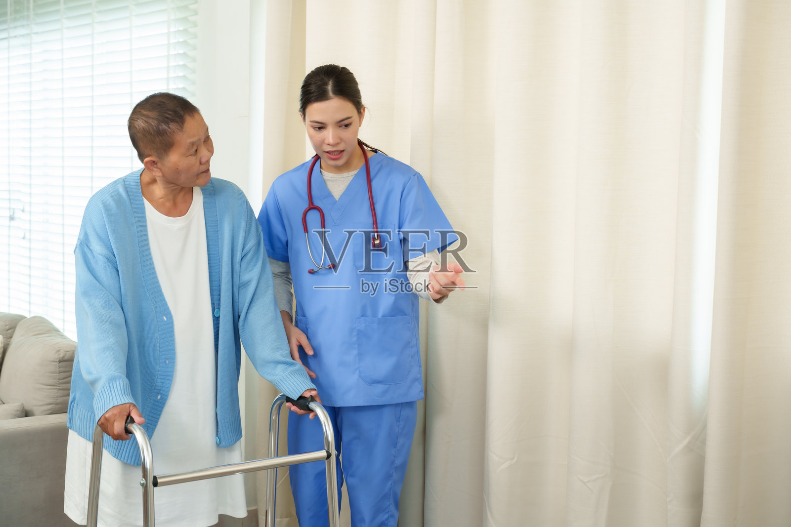 护士在家庭物理治疗课程中指导使用助行器的老年女性。强调关怀护理、行动支持以及对患者康复和健康的鼓励。照片摄影图片