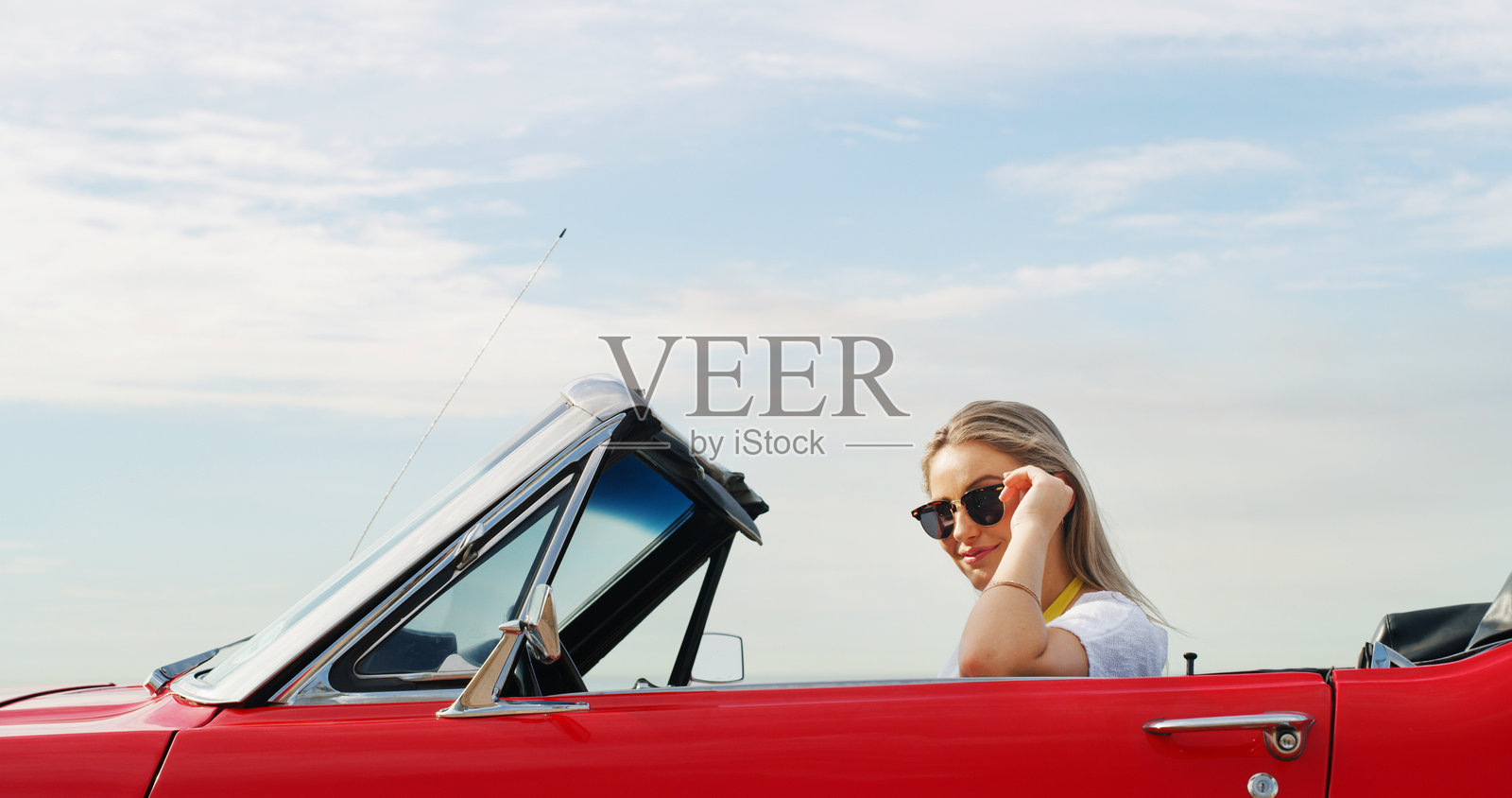 女性在敞篷车中佩戴太阳镜，享受蓝天的公路旅行，冒险、休息或旅行。假期、夏季和度假，户外运动汽车中的人进行驾驶、旅程或交通。照片摄影图片