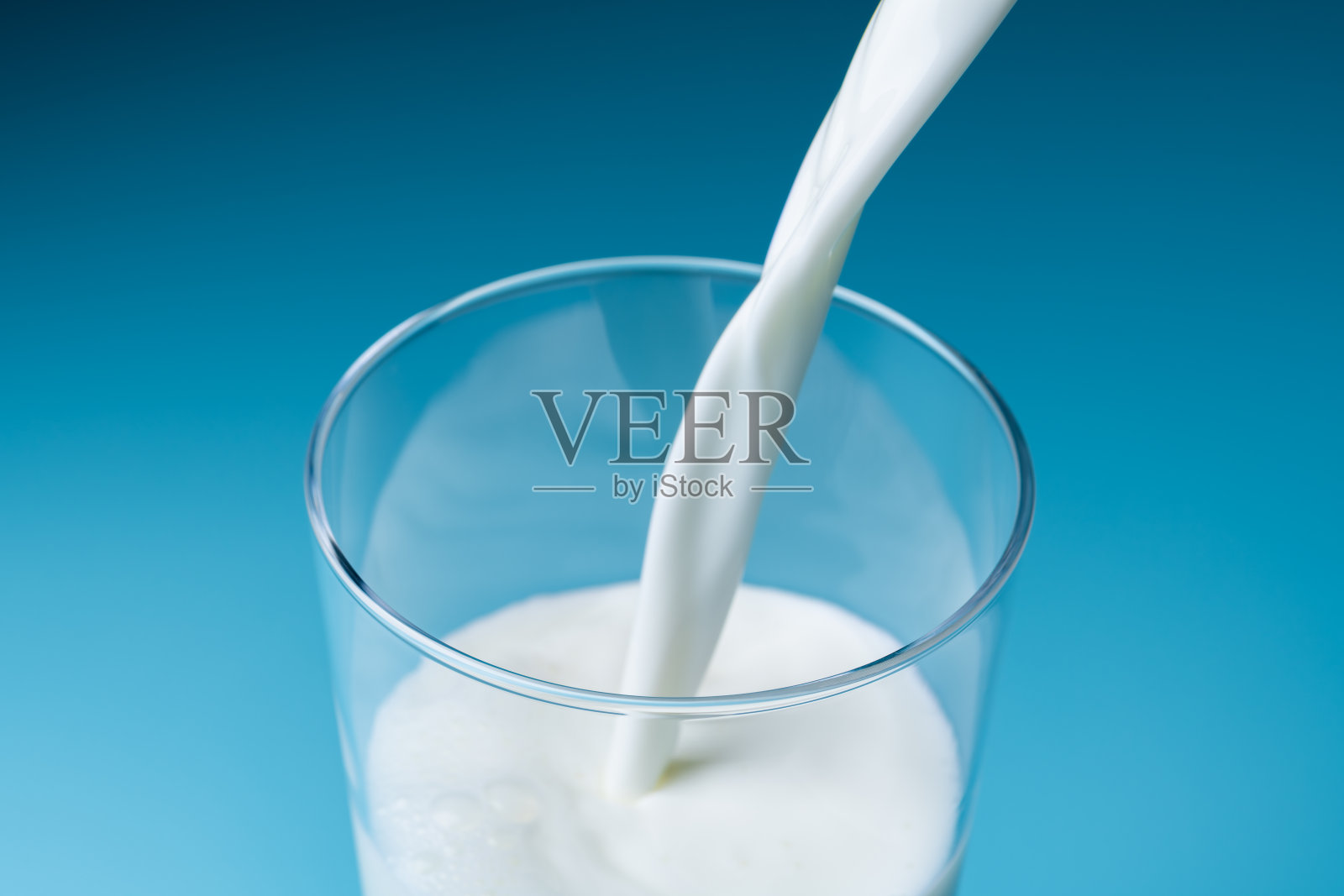 在蓝色背景前将牛奶倒入玻璃杯中照片摄影图片