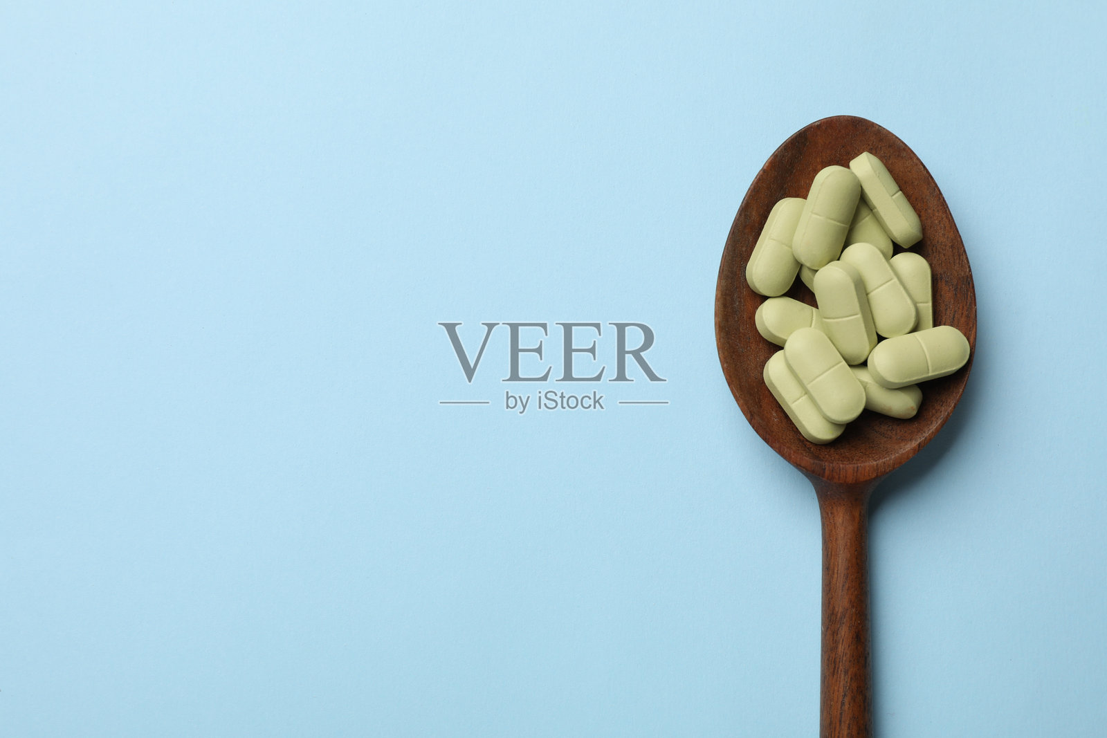 浅蓝色背景上的木勺里装着维生素药丸，俯视图。留白以便添加文字。照片摄影图片