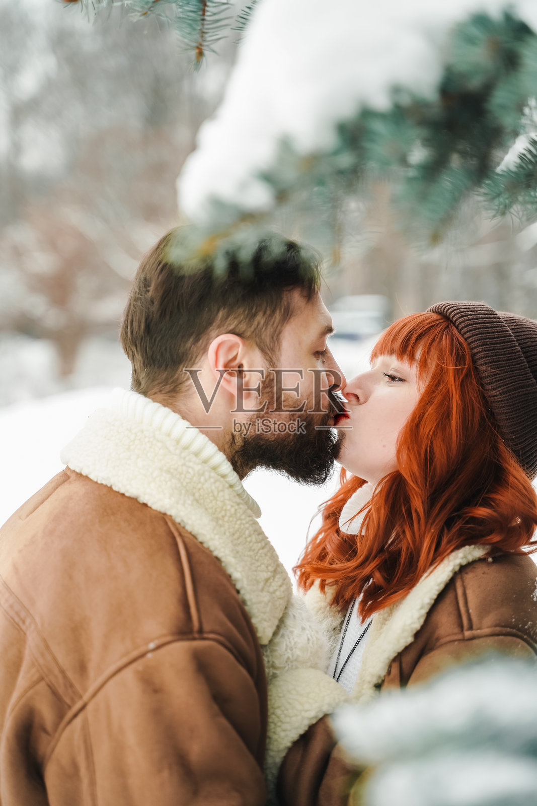 浪漫情侣爱情故事。粗犷的胡子男人，明亮的红发女孩在冬季公园。浪漫约会，亲吻，拥抱。散步，玩乐。时尚服装，红色羊皮大衣，夹克，帽子。照片摄影图片