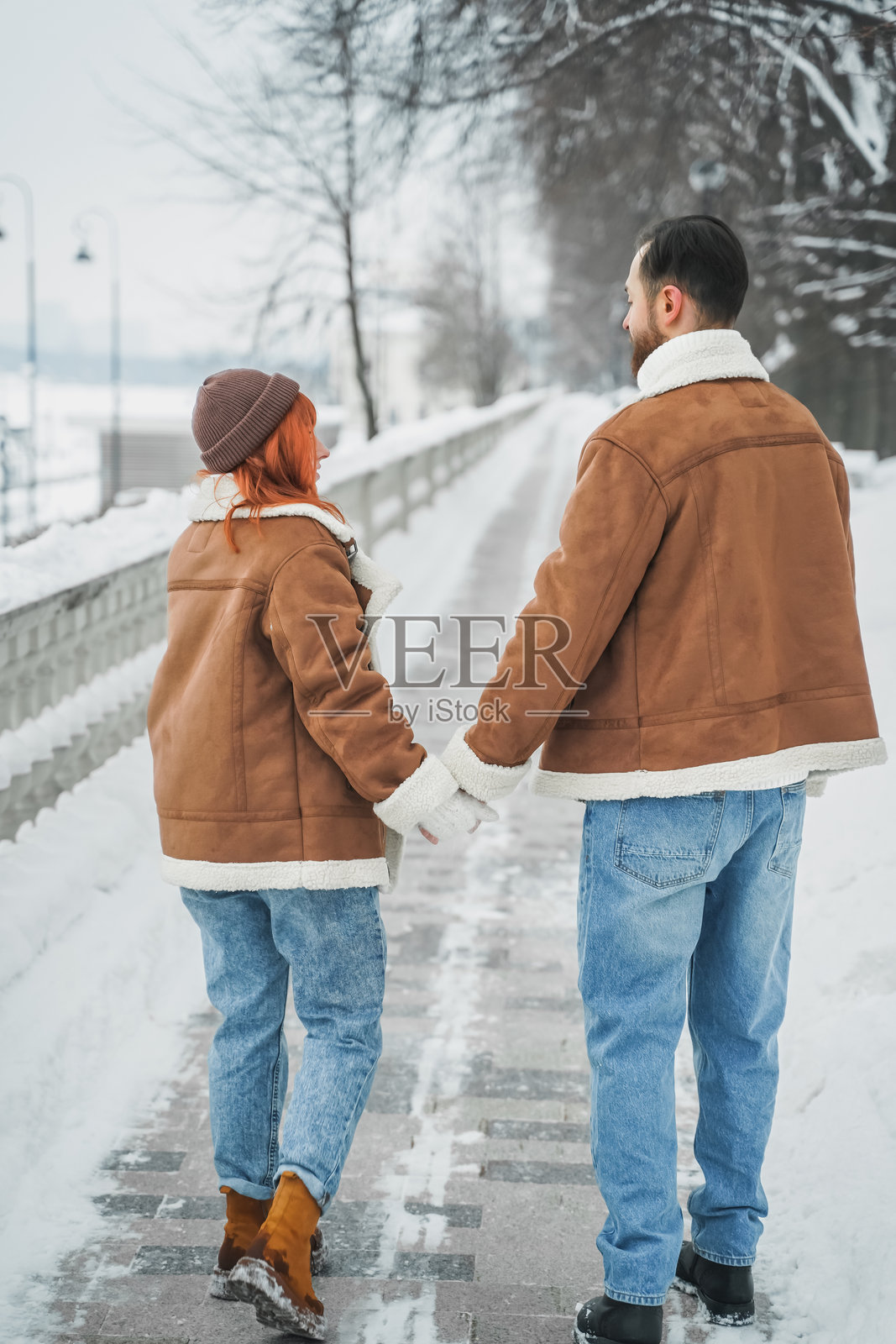 浪漫情侣爱情故事。一个粗犷的胡子男人和一个明亮红发的女孩在冬季公园。浪漫约会，亲吻，拥抱。散步，玩乐。时尚服装，红色羊皮大衣，夹克，帽子。照片摄影图片