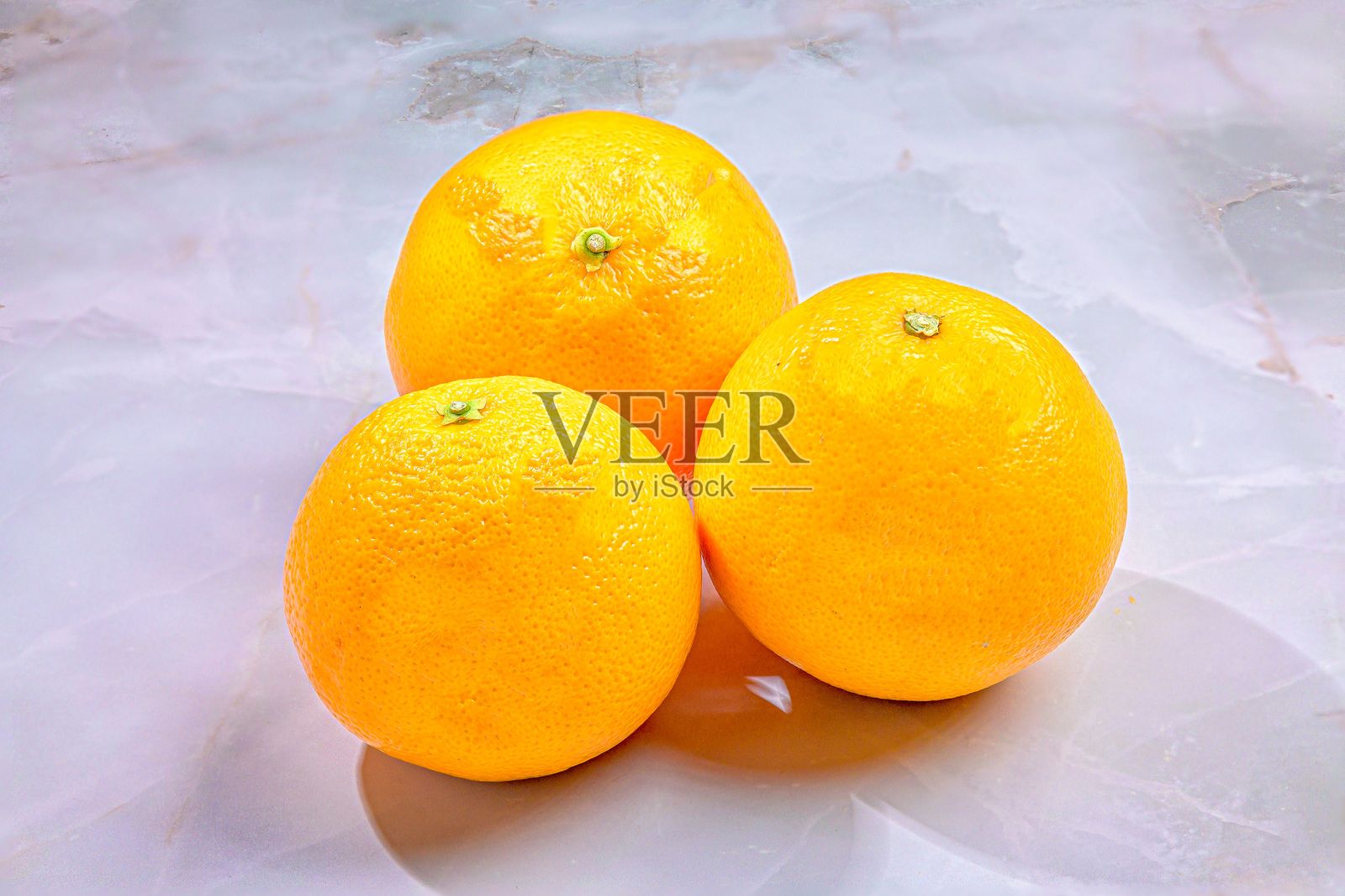 三颗明亮的橙子在光滑的大理石表面上形成简约的构图。照片摄影图片
