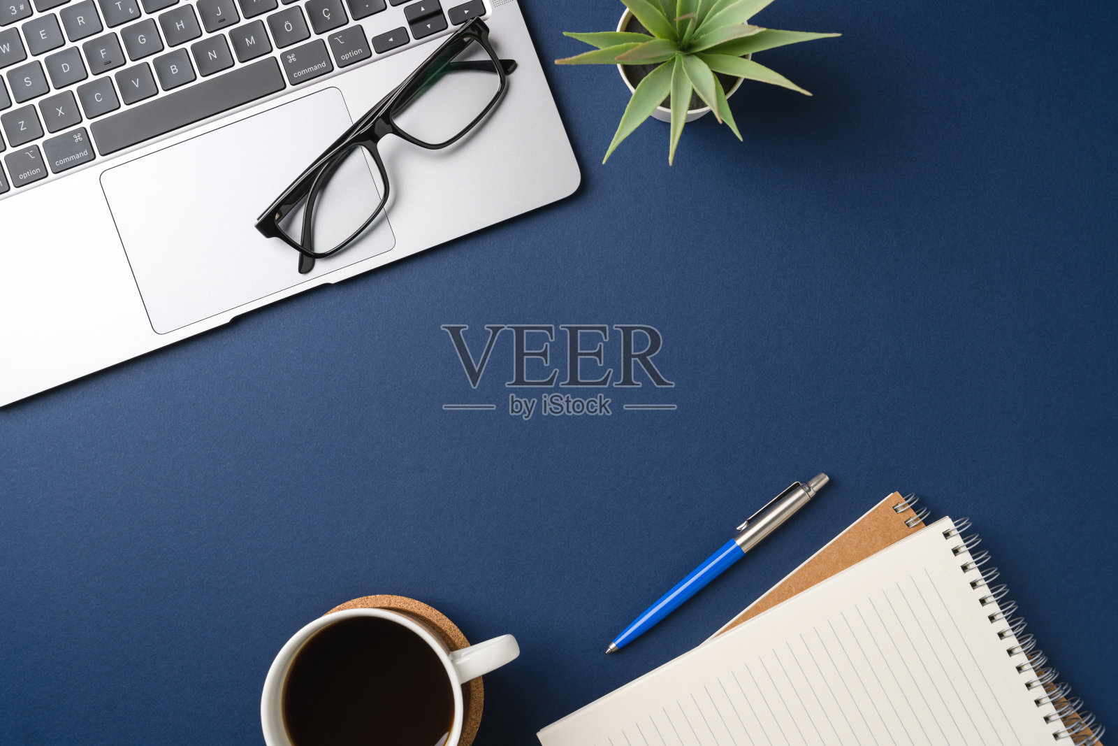 带有键盘、笔记本电脑、办公用品、钢笔、绿叶和咖啡杯的工作区。平铺，俯视蓝色办公桌。照片摄影图片