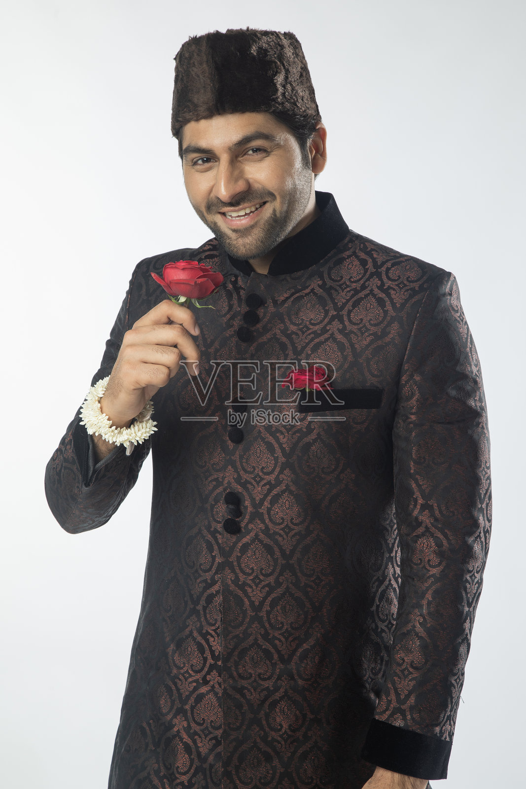 身穿传统服装的快乐新郎手捧玫瑰，背景为白色。照片摄影图片