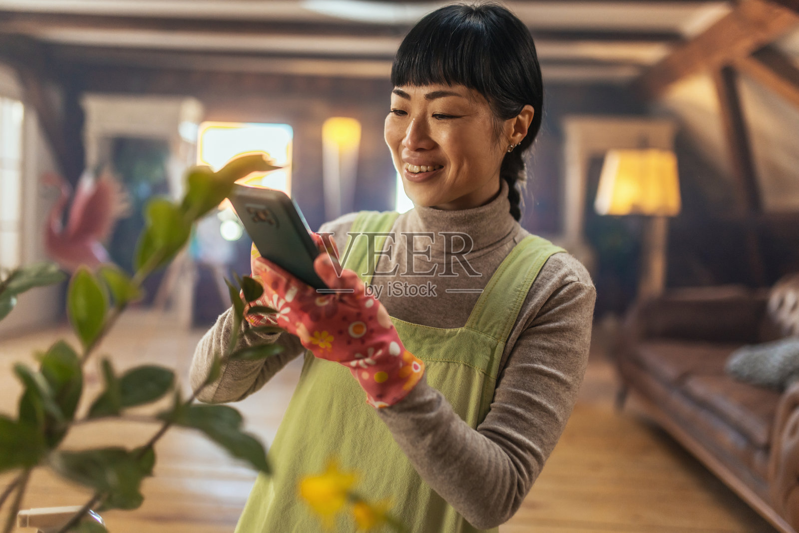 一位年轻的日本女性愉快地在室内照料她的盆栽植物，周围环绕着绿色植物。她温馨的家居环境体现了对园艺的热爱。照片摄影图片