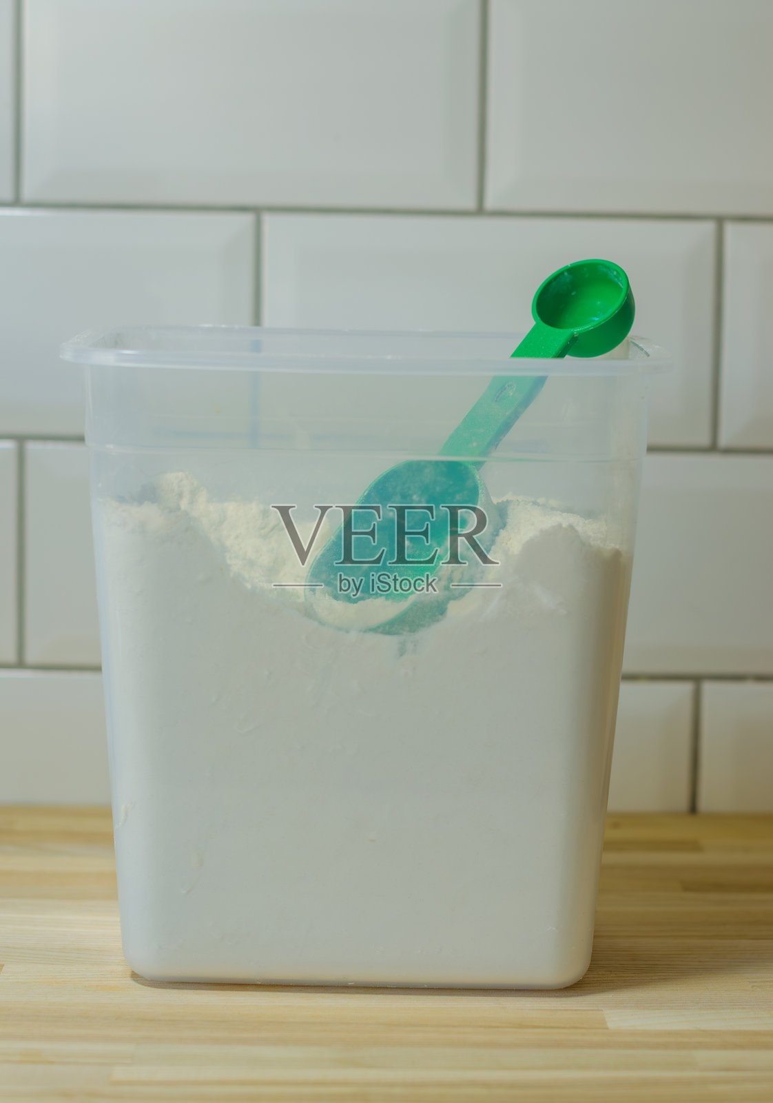 透明容器中的面粉，配有绿色铲子，厨房内有白色标题照片摄影图片