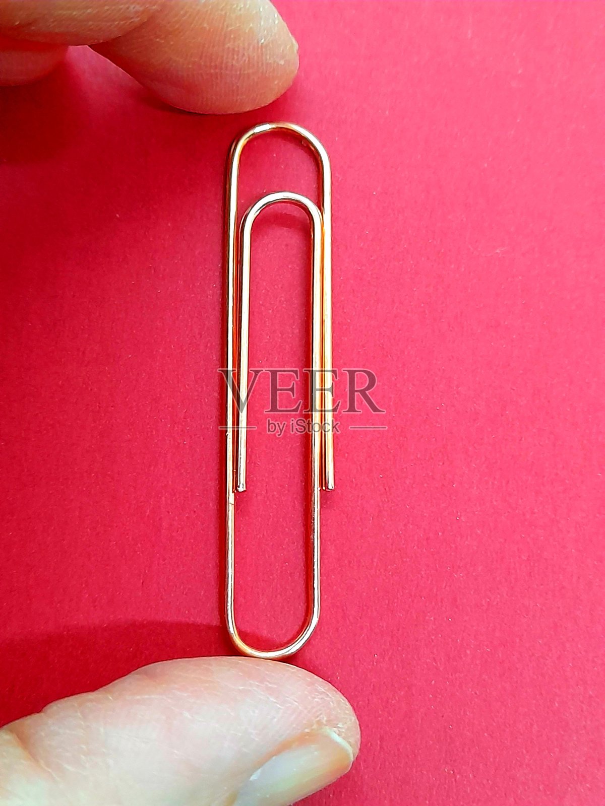 手中握着一个大金色回形针。照片摄影图片