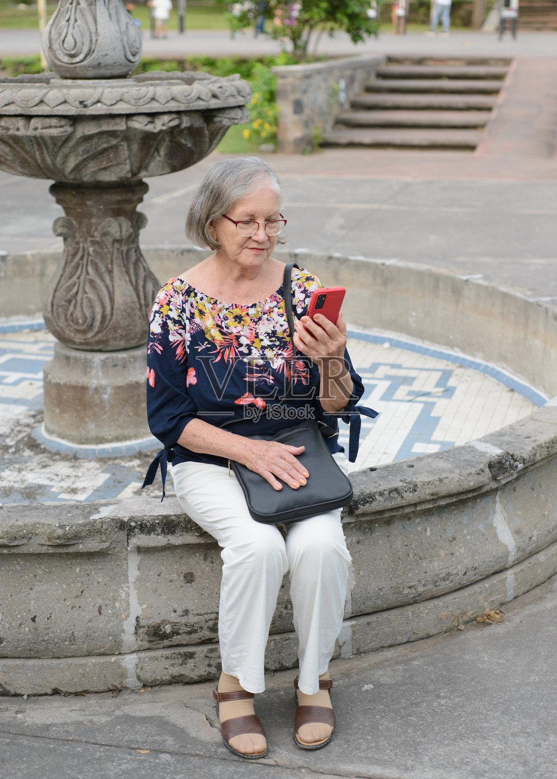 一位年长女性坐在公园里用手机进行视频通话照片摄影图片