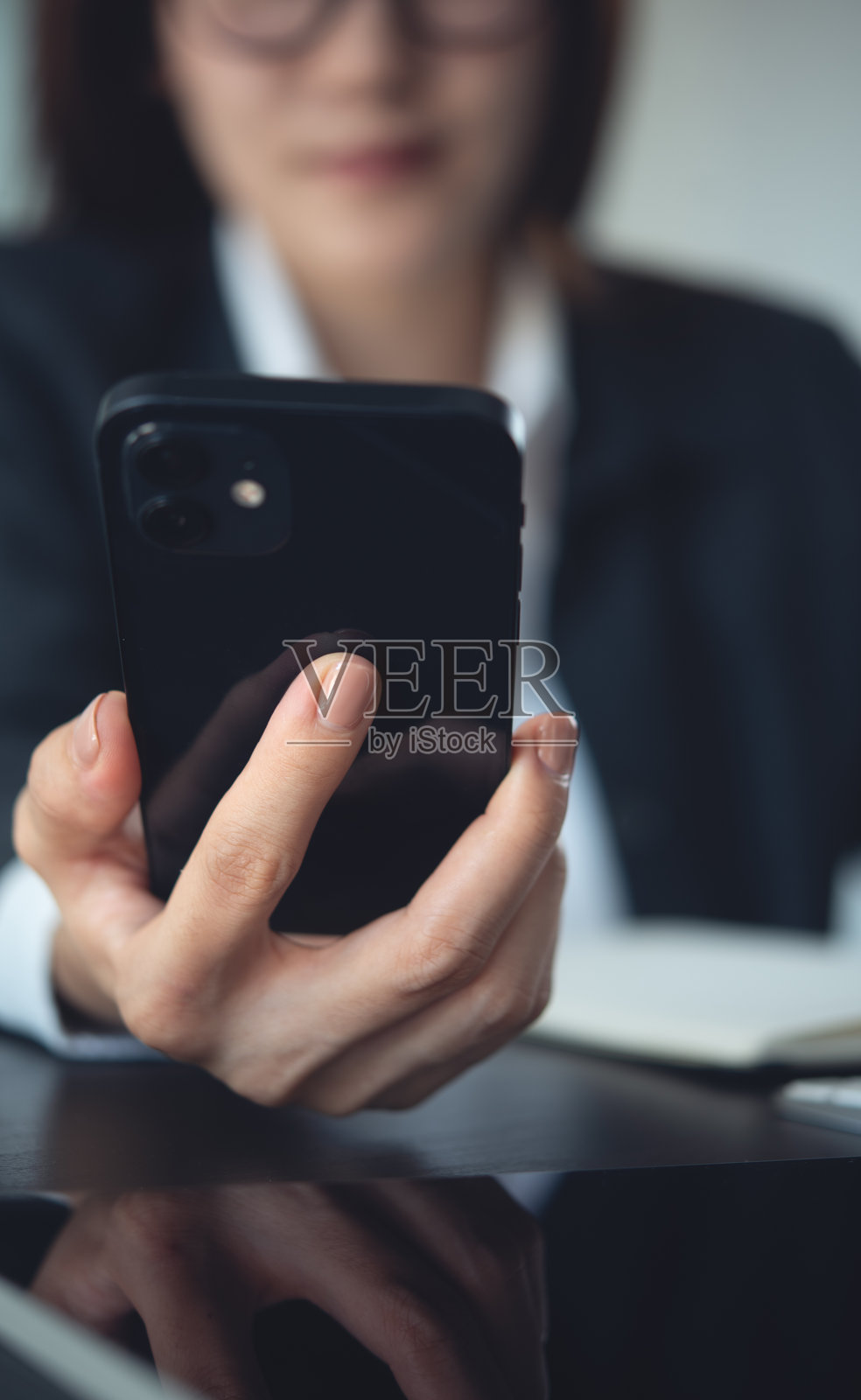 特写，女商人在办公室使用手机，正在笔记本电脑上工作。女商人的手拿着手机，在线研究电脑设备，背景为商务环境。照片摄影图片