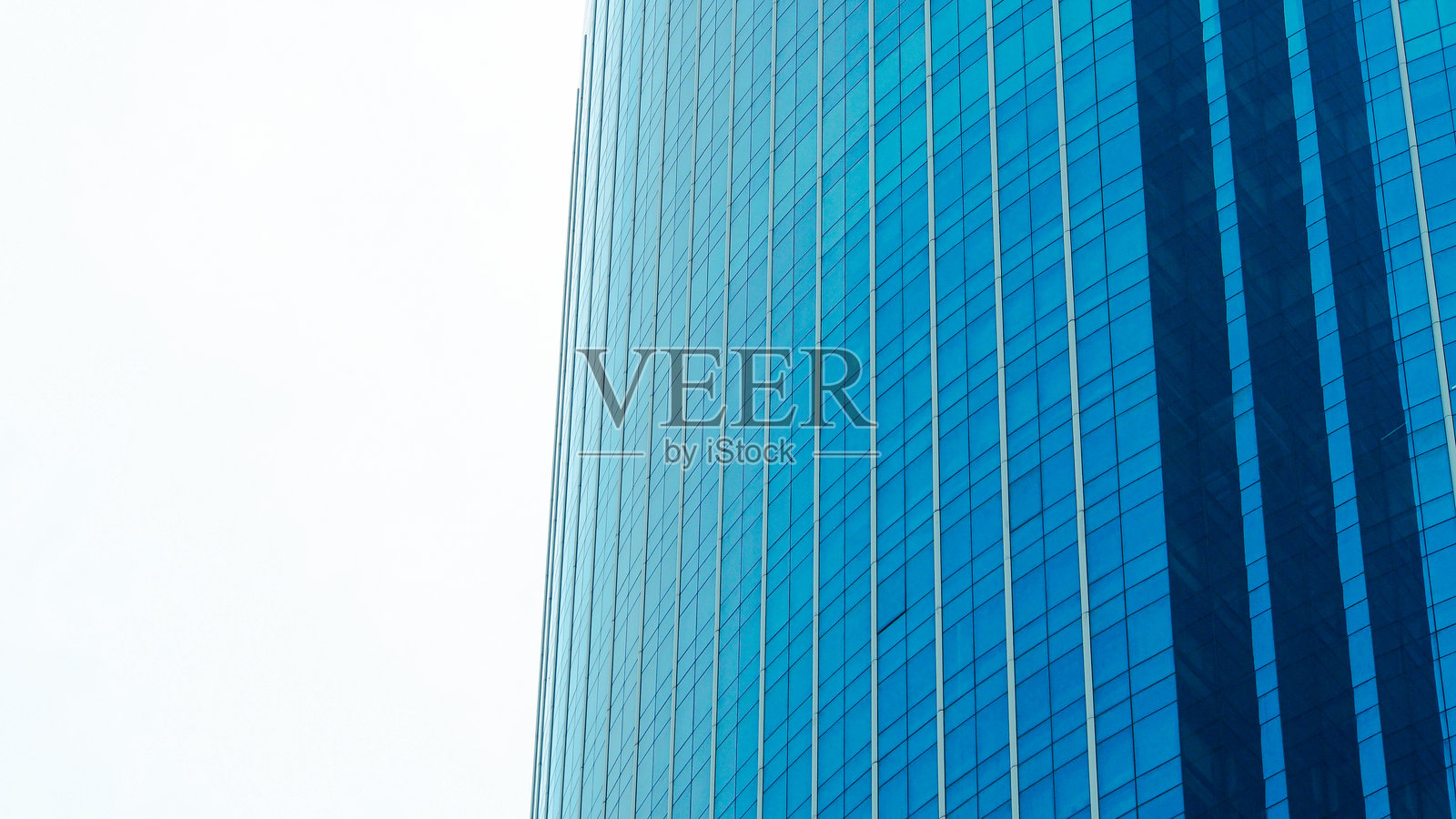 现代玻璃摩天大楼建筑。低角度拍摄的弯曲蓝色玻璃外立面反射着天空和城市景观。照片摄影图片