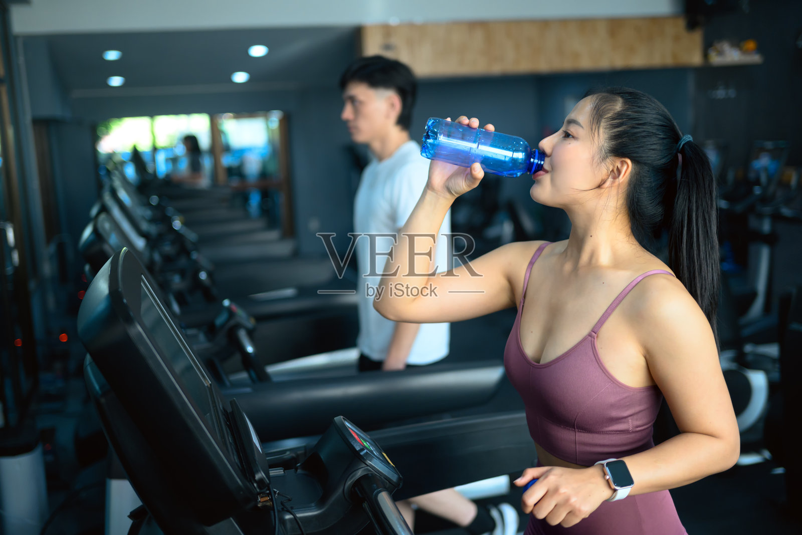 吸引人的女性在跑步机上锻炼时与健身伙伴一起喝水照片摄影图片