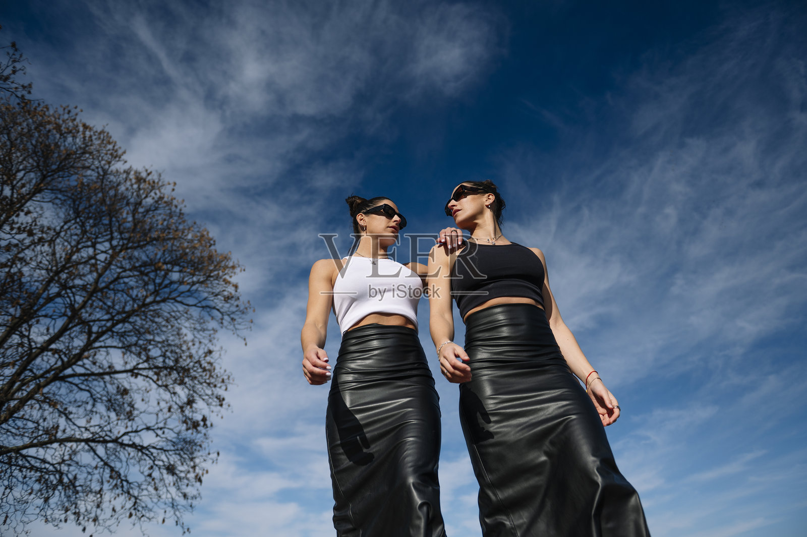 两位时尚女性在阳光明媚的天空下自信地走着，融合了现代优雅与大胆态度。照片摄影图片