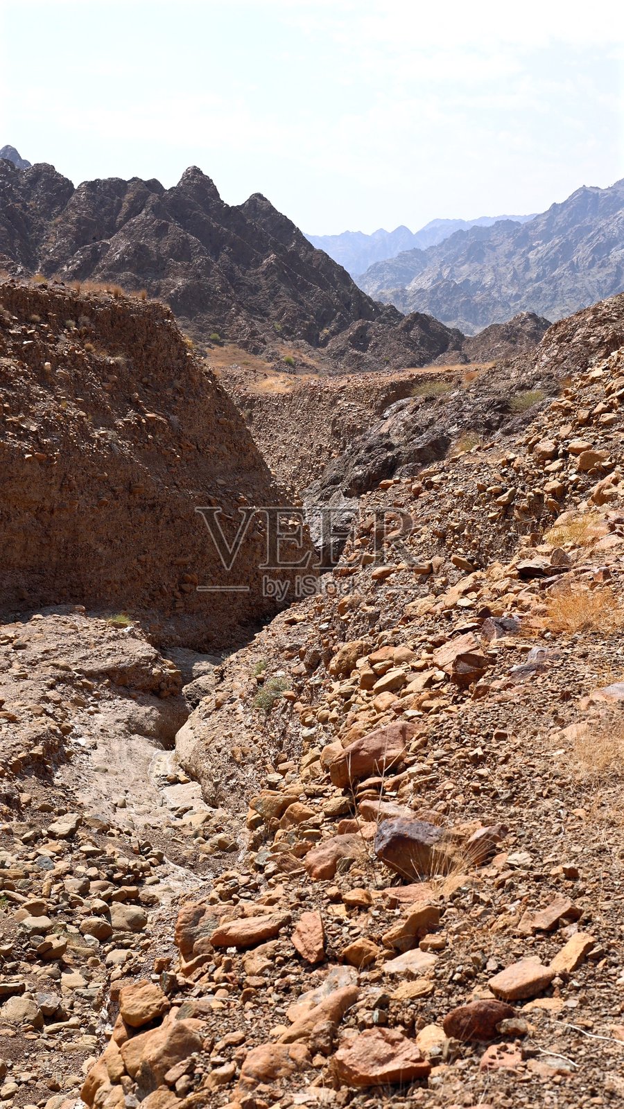 岩石悬崖环绕着山脉，岩石小径穿过侵蚀雕刻的地貌，侵蚀形成深邃的通道，探险者在岩石小径上探索，山脉在侵蚀的岩层之外高耸。照片摄影图片