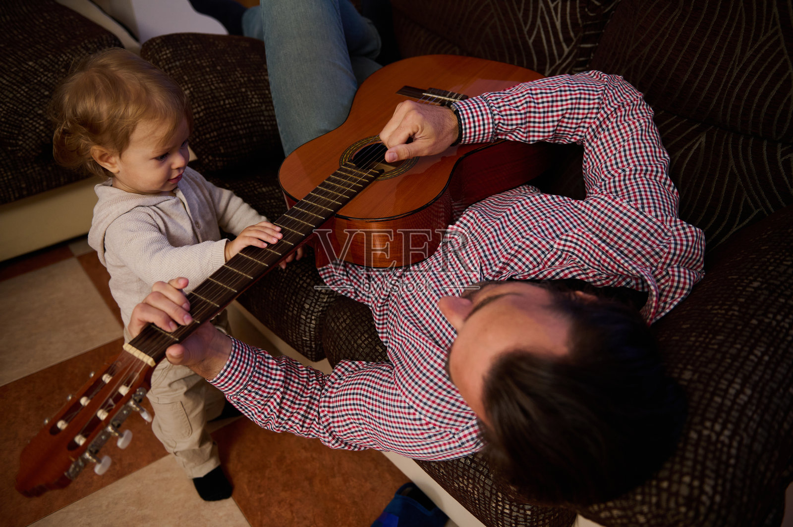 父亲和孩子在温馨的客厅里一起弹吉他，增进感情。照片摄影图片
