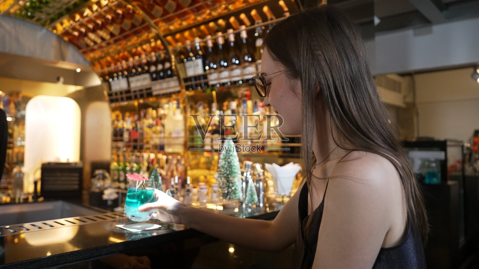 美丽的女人在品尝圣诞蓝色泻湖鸡尾酒主题时拉上拉链。照片摄影图片