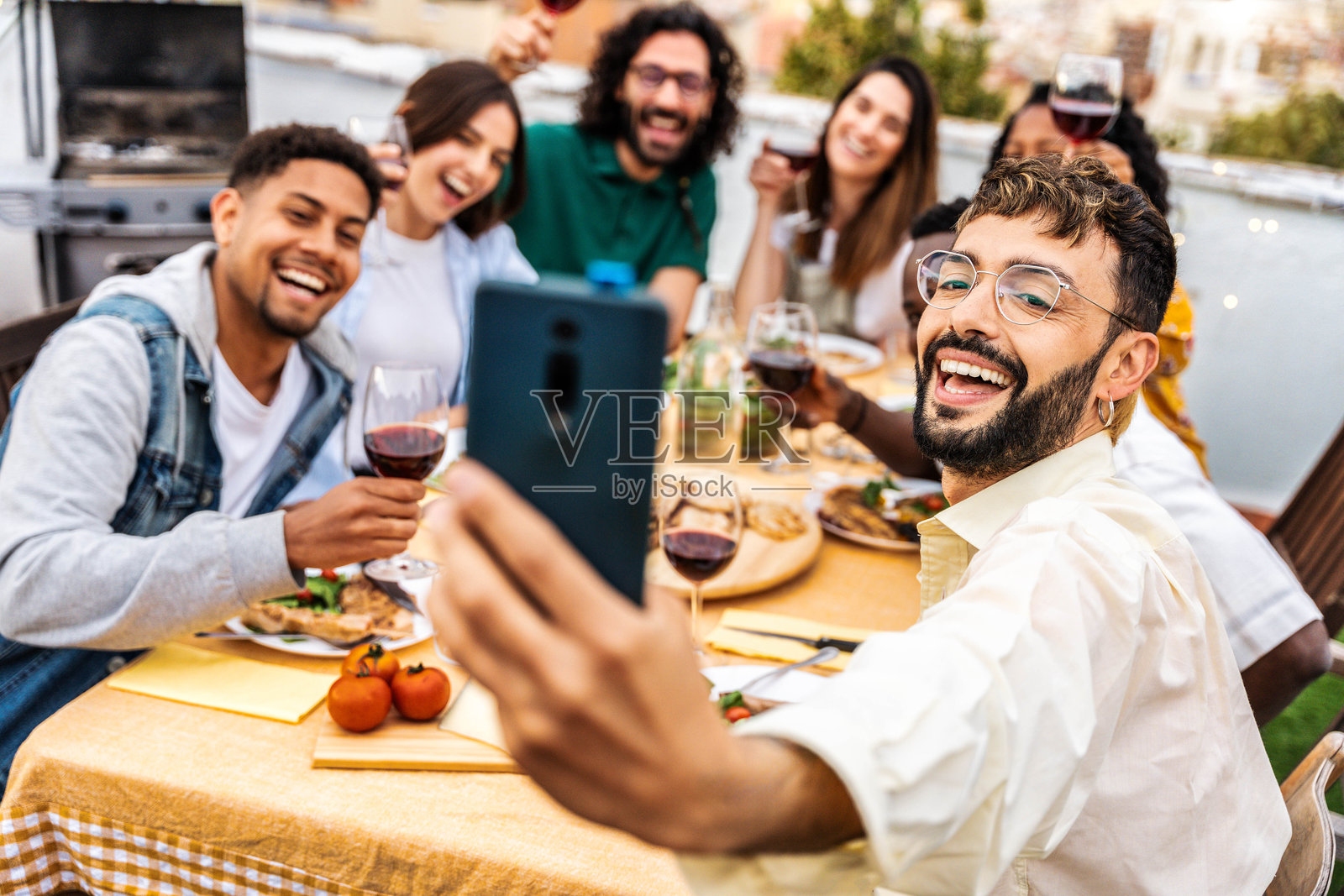 快乐的朋友们在屋顶晚宴派对上尽情享受 - 一群年轻人在户外餐桌上拍自拍照 - 生活方式概念，男孩女孩们一起吃饭喝酒照片摄影图片