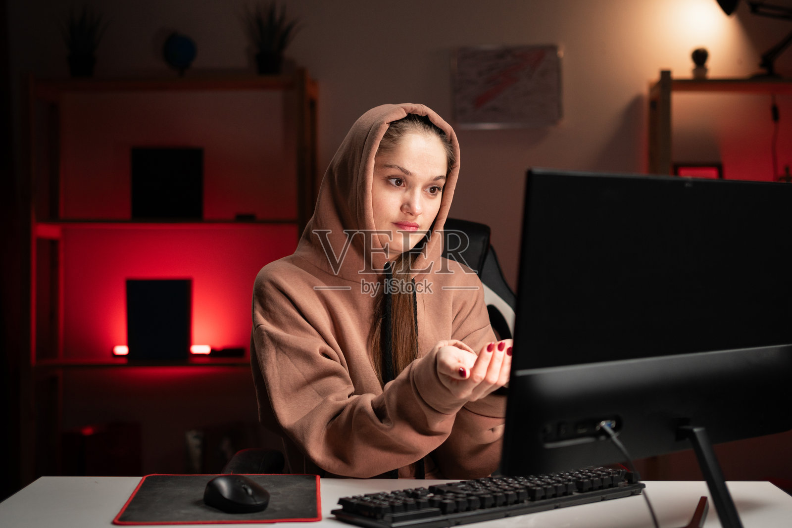 年轻漂亮的程序员穿着连帽衫，在家里熬夜加班，双手合十恳求帮助。照片摄影图片