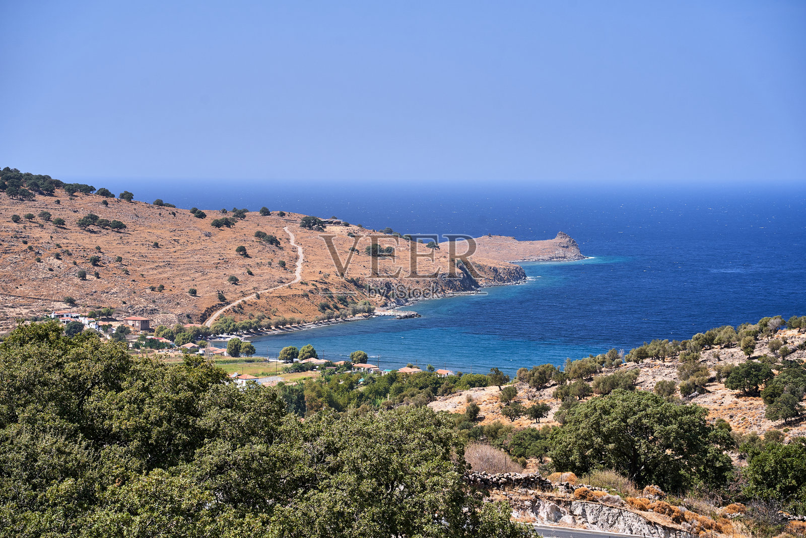 莱斯博斯岛上岩石海岸的山丘、树木和房屋照片摄影图片