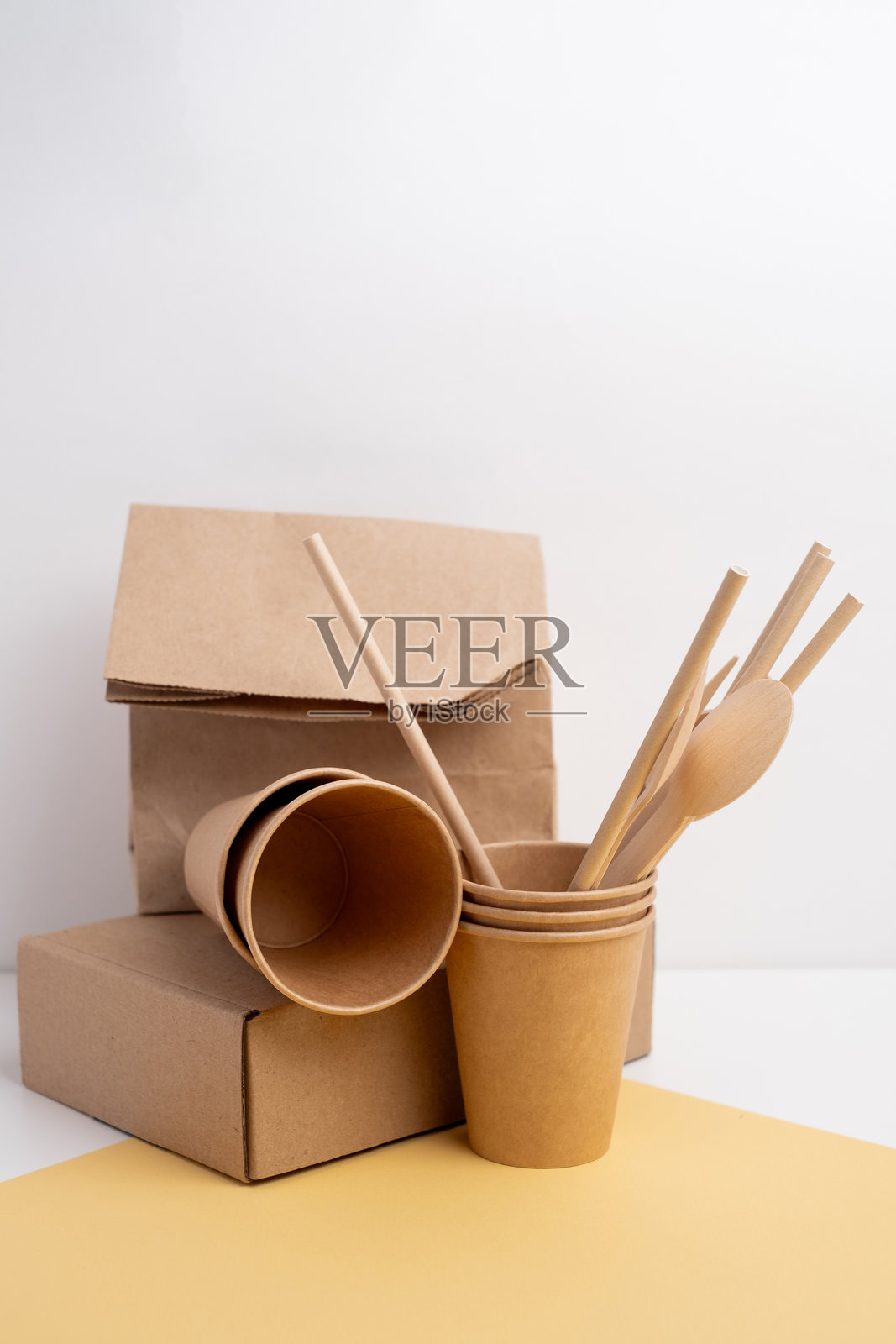 一堆环保一次性餐具。木制叉子和刀子，纸杯和纸盘在浅色背景上。适合野餐和外卖食品的可生物降解餐具和餐盘。照片摄影图片