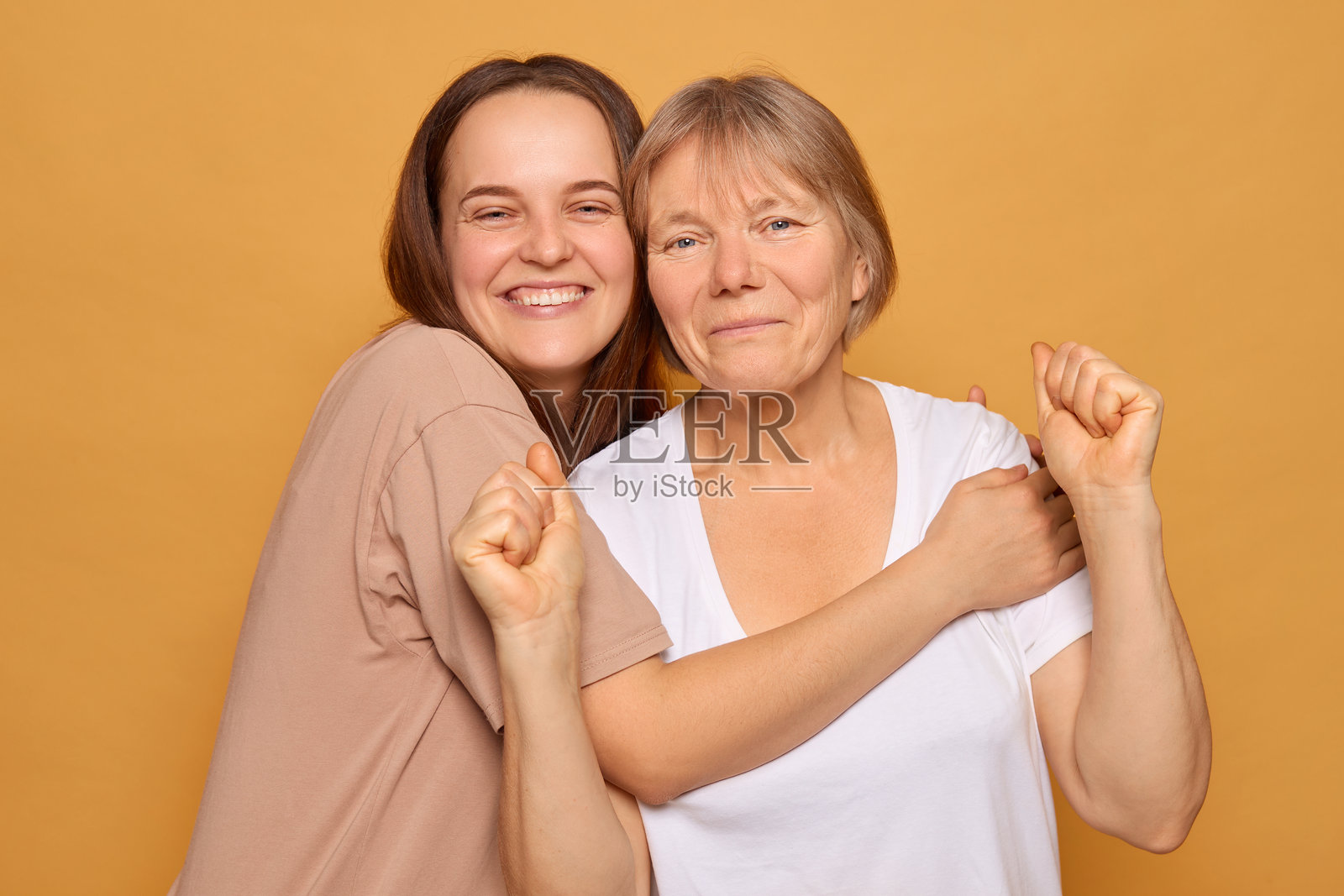 两位女性表达着快乐，互相拥抱，面带灿烂的笑容。她们在鲜艳的黄色背景前享受着无忧无虑的时刻，散发着温暖和积极的气息。照片摄影图片