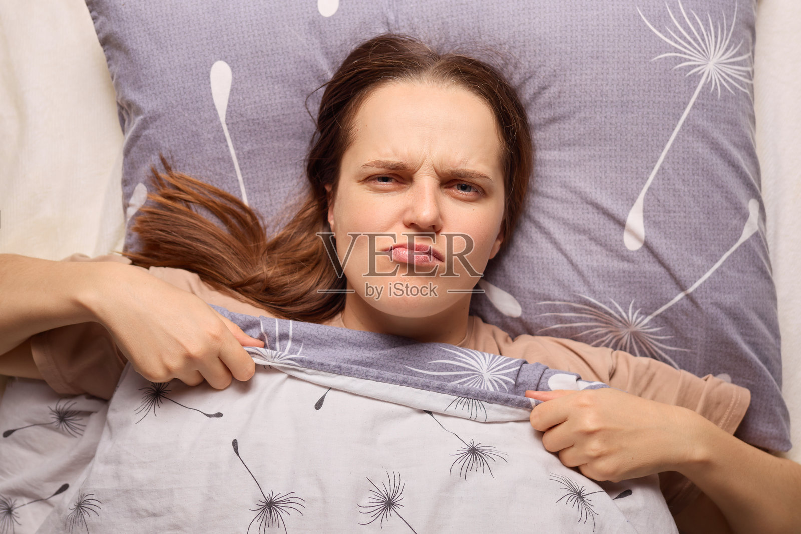 一位女性躺在床上，面露不悦，试图扯掉被子，正应对懒散的早晨。氛围暗示着她渴望赖床。照片摄影图片