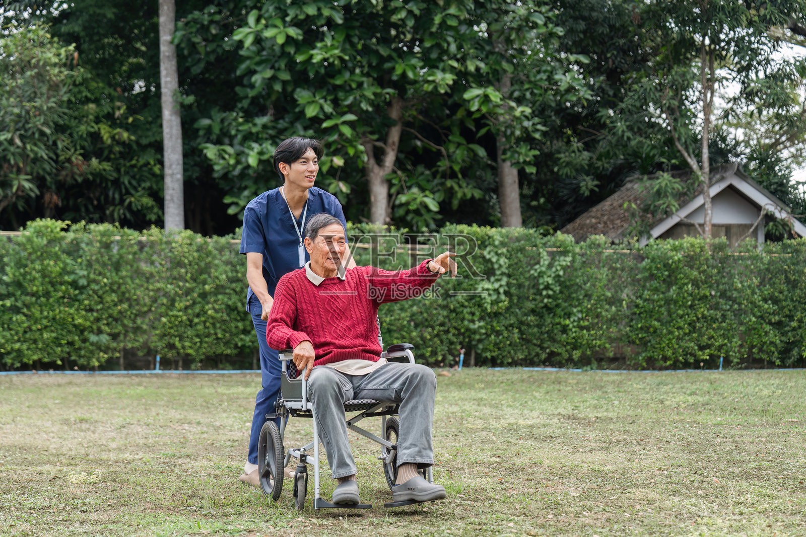 医疗专业人员推着一位老年男子的轮椅，在宁静的花园中欣赏美丽的风景照片摄影图片