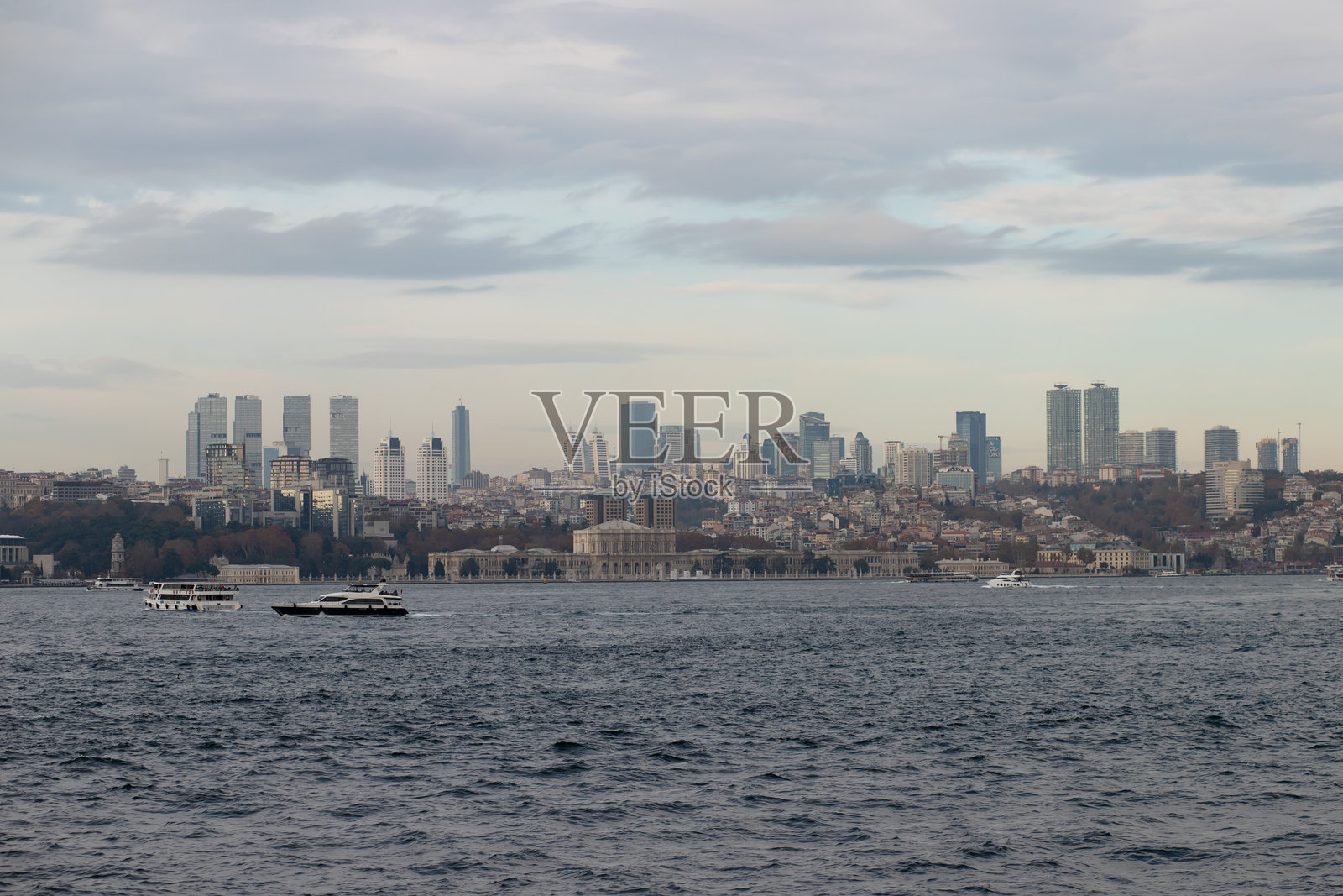 现代高楼、历史地标和水边活动的城市天际线，平静海面上的船只在多云的天空下，土耳其伊斯坦布尔，2024年11月20日照片摄影图片