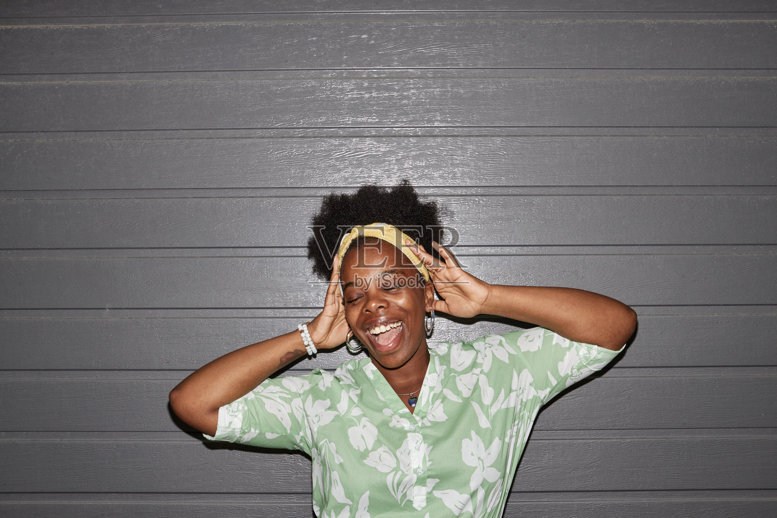 时尚快乐的女性在灰色墙前摆姿势，双臂高举照片摄影图片