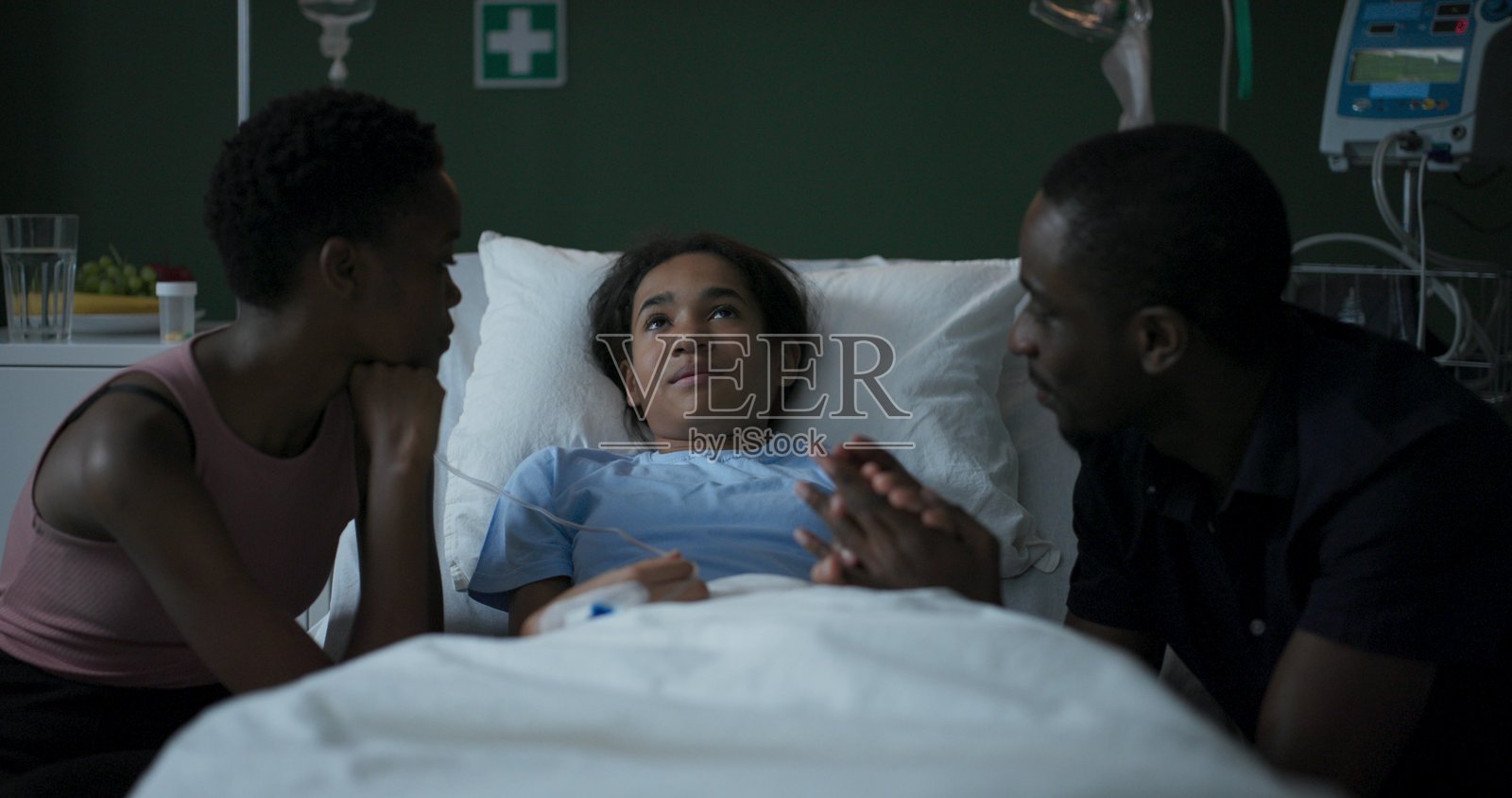 非洲父母坐在医院病房里，陪伴着正在接受重病治疗的女儿。照片摄影图片