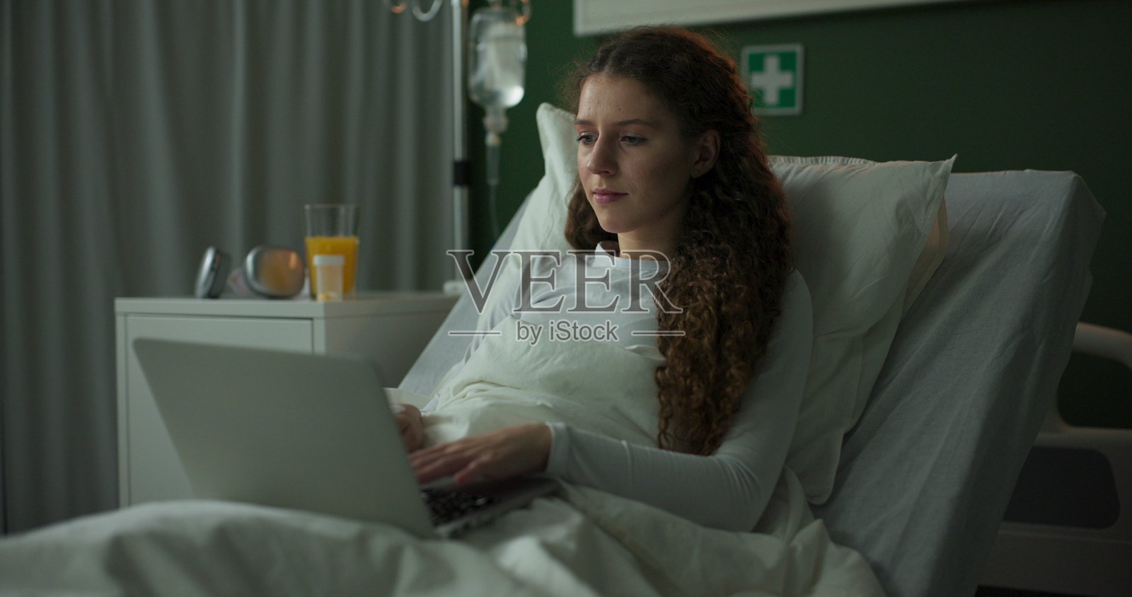 年轻女孩在医院病床上微笑着与亲人视频通话照片摄影图片