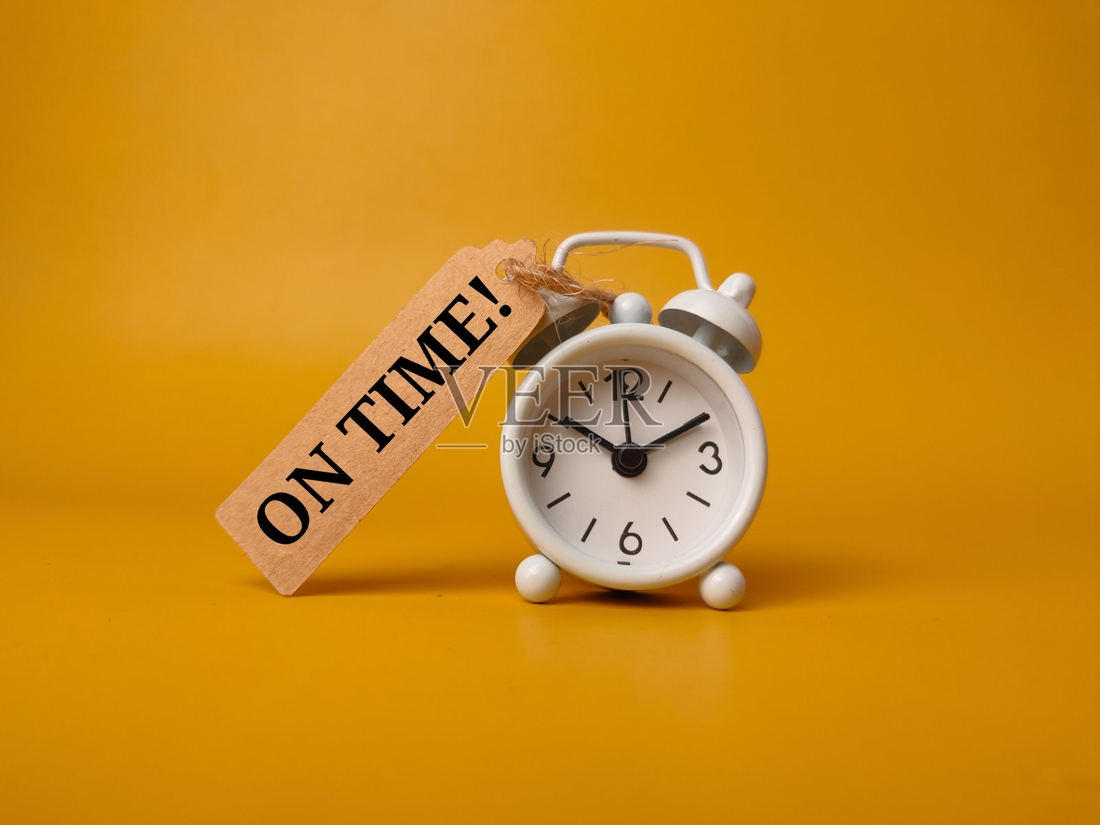 闹钟和一张写有“准时”的棕色卡片，背景为黄色照片摄影图片
