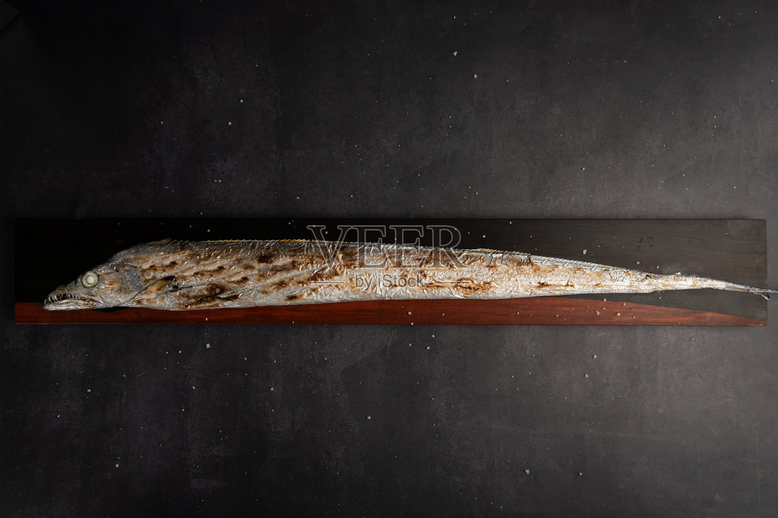 黑色背景上的木砧板上的烤鱼。照片摄影图片