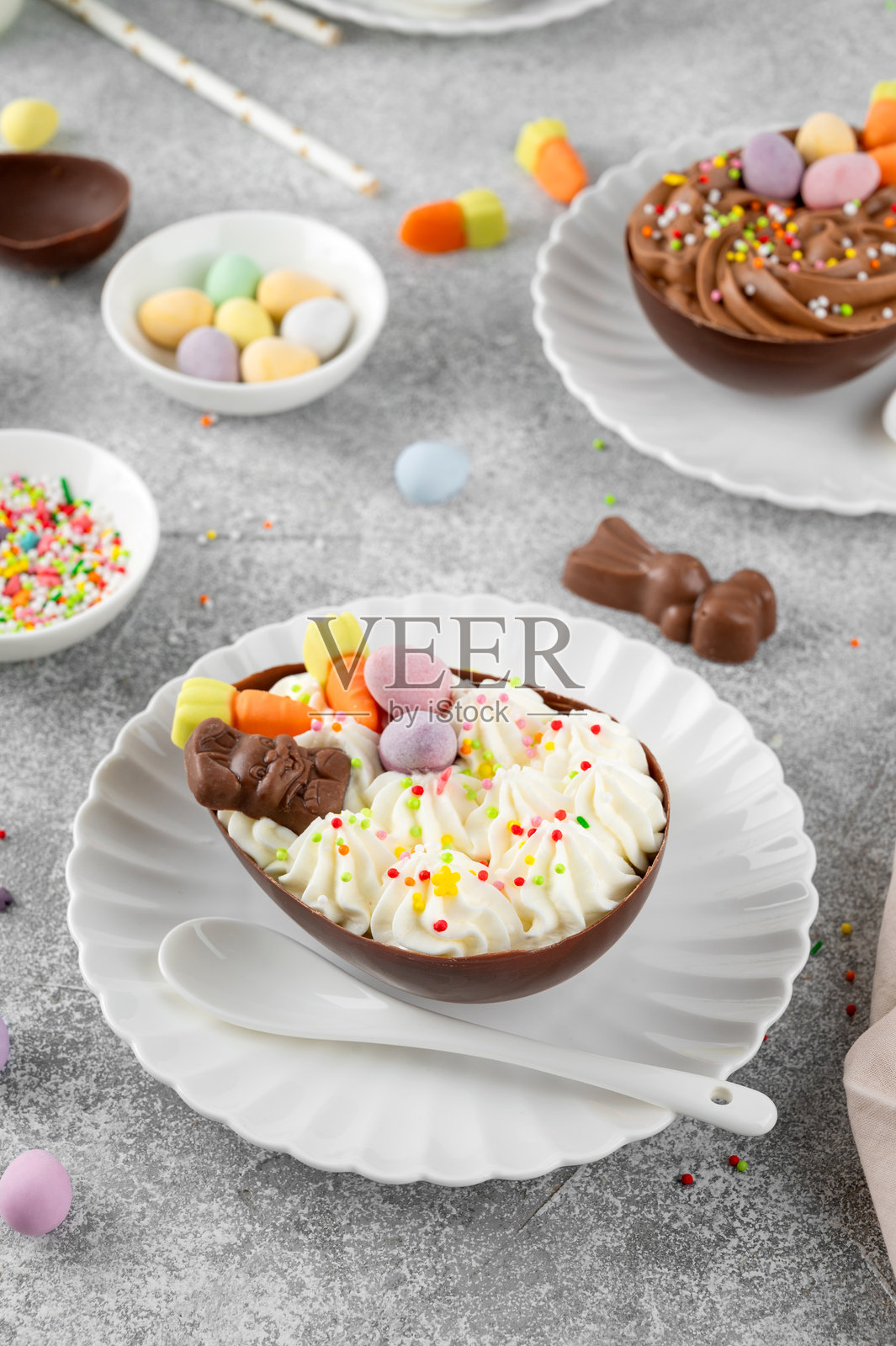 复活节甜点。白色盘子上放着巧克力蛋，里面填充了奶酪蛋糕，装饰有巧克力糖果和糖霜，背景为灰色混凝土。留白空间。照片摄影图片