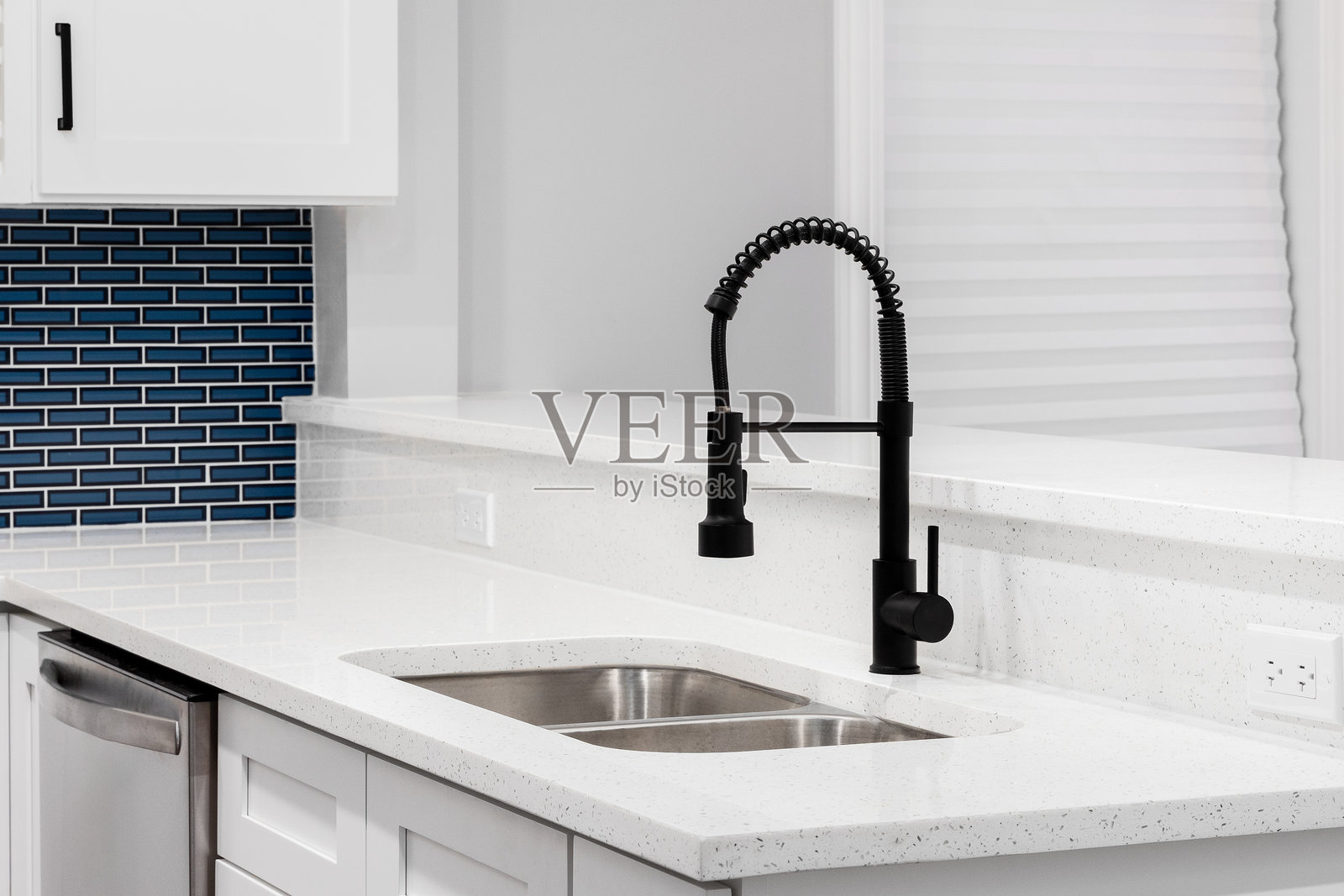 白色厨房中的黑色水龙头，配有蓝色地铁瓷砖背墙。照片摄影图片