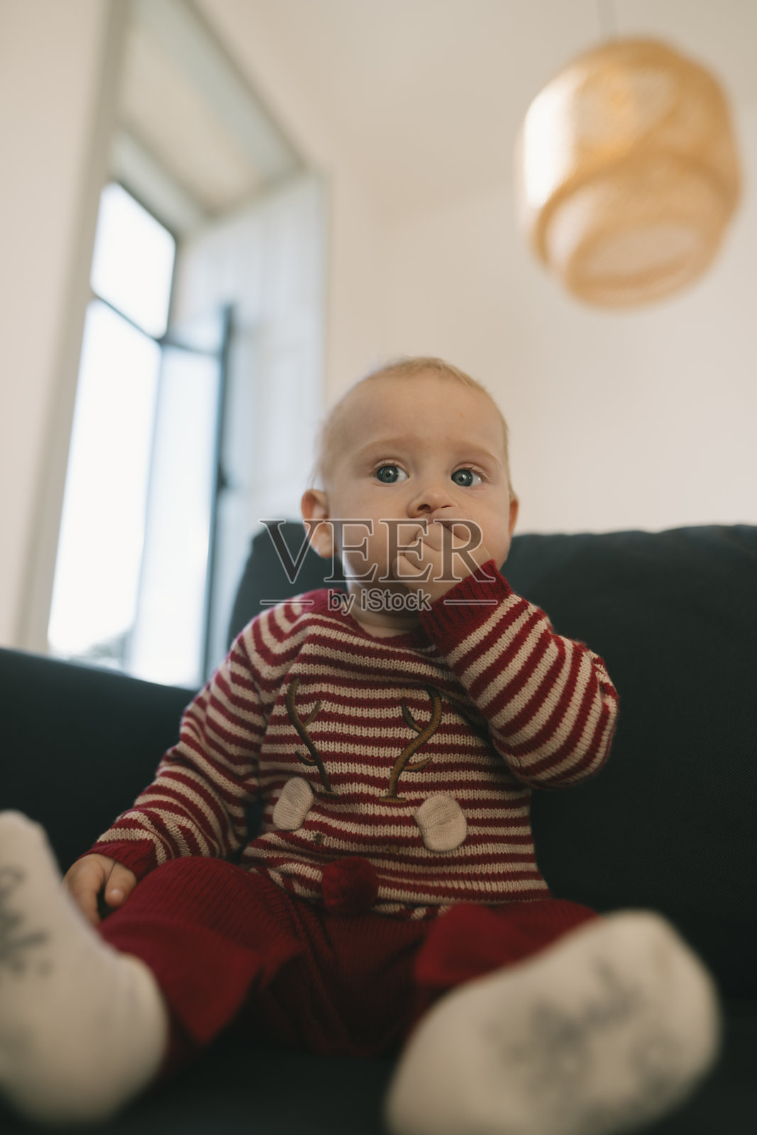 穿着柔软条纹睡衣的可爱宝宝在室内舒适地坐着，满脸喜悦。照片摄影图片
