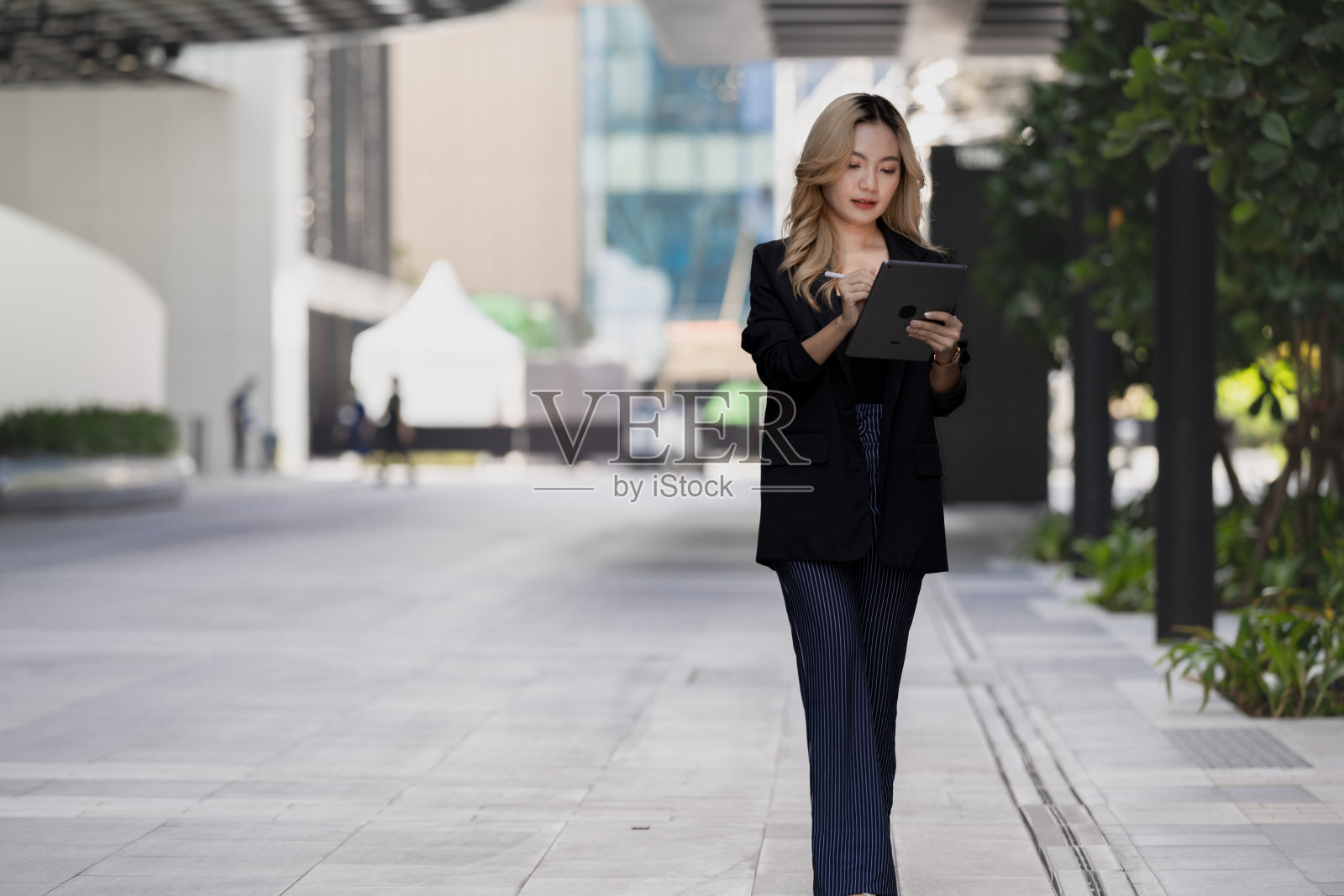 自信的女商人手持平板电脑和触控笔，强调在现代工作空间中的精准与适应性，融合了风格与功能性。照片摄影图片