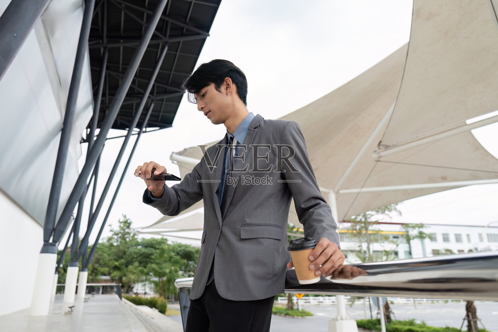 年轻的亚洲商人在户外穿着西装，一边喝着咖啡，一边查看智能手机。照片摄影图片