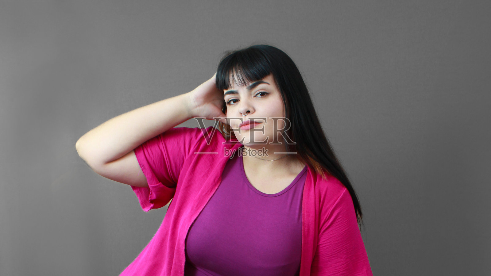 美丽的白肤女性，穿着紫色衬衫和粉色开衫，一只手放在头上摆姿势。照片摄影图片